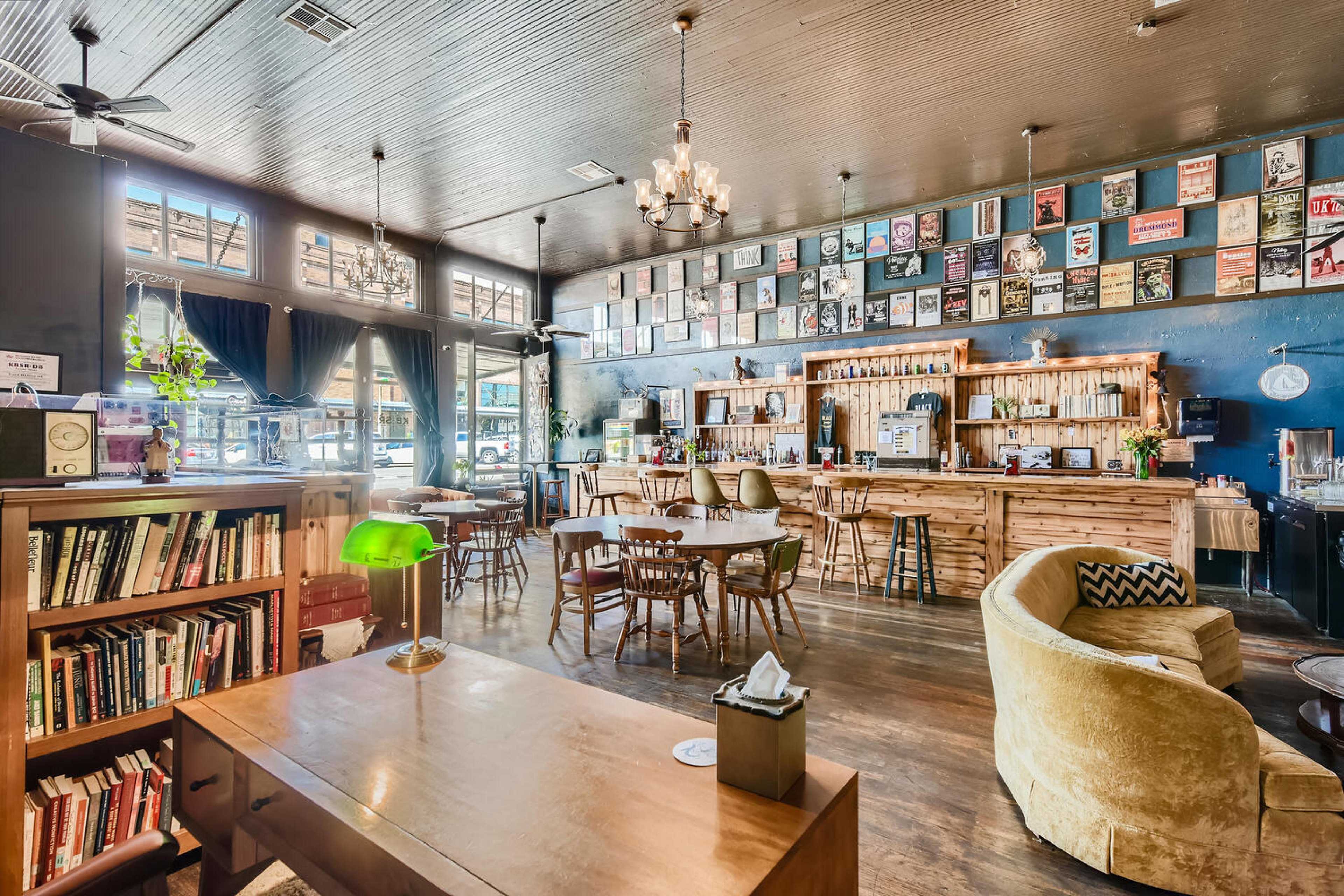 A cozy café interior with a wooden bar, bookshelves, and walls adorned with framed posters.