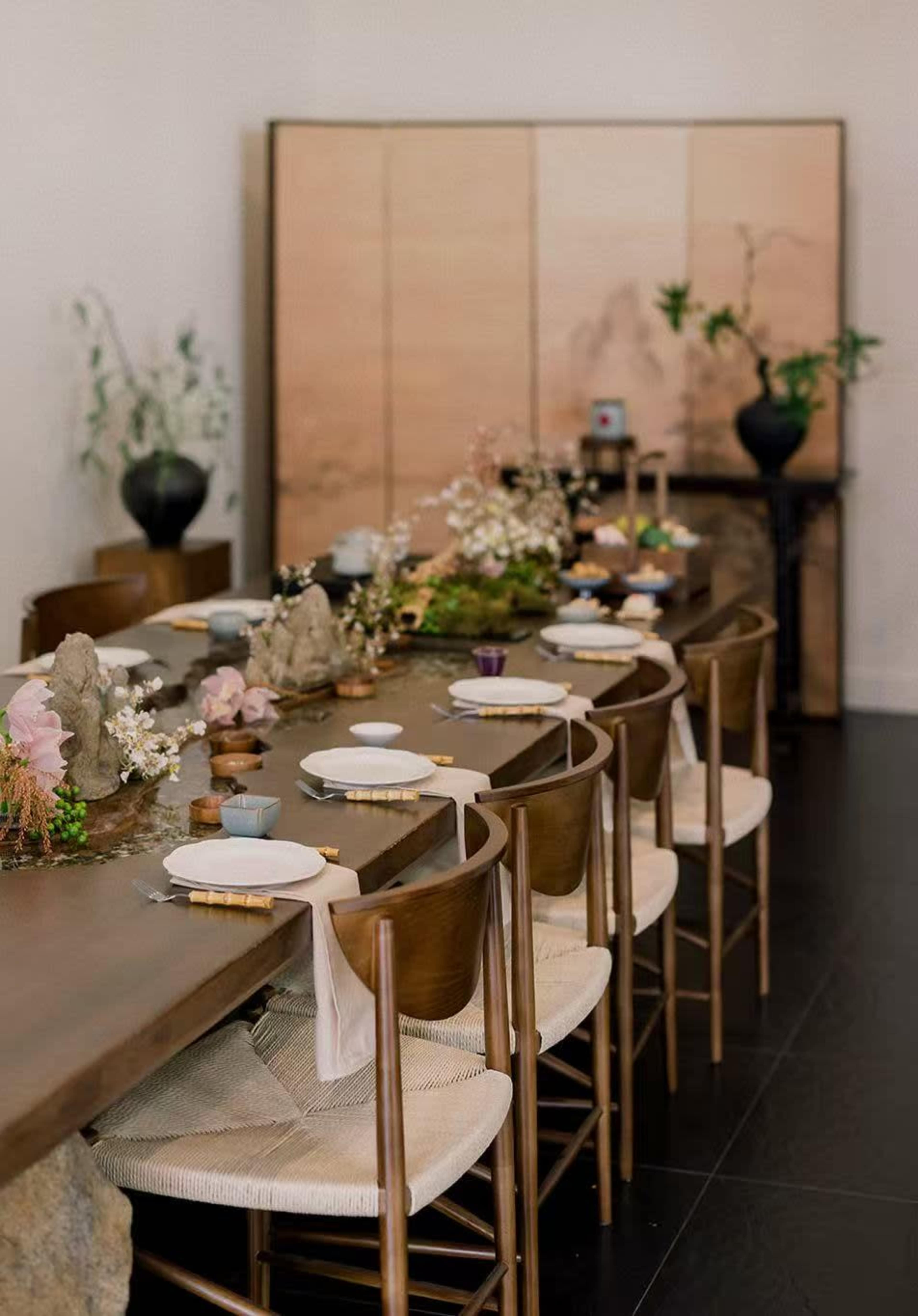 A long wooden dining table is set with dishware and decorative elements in a modern, minimalist dining room.