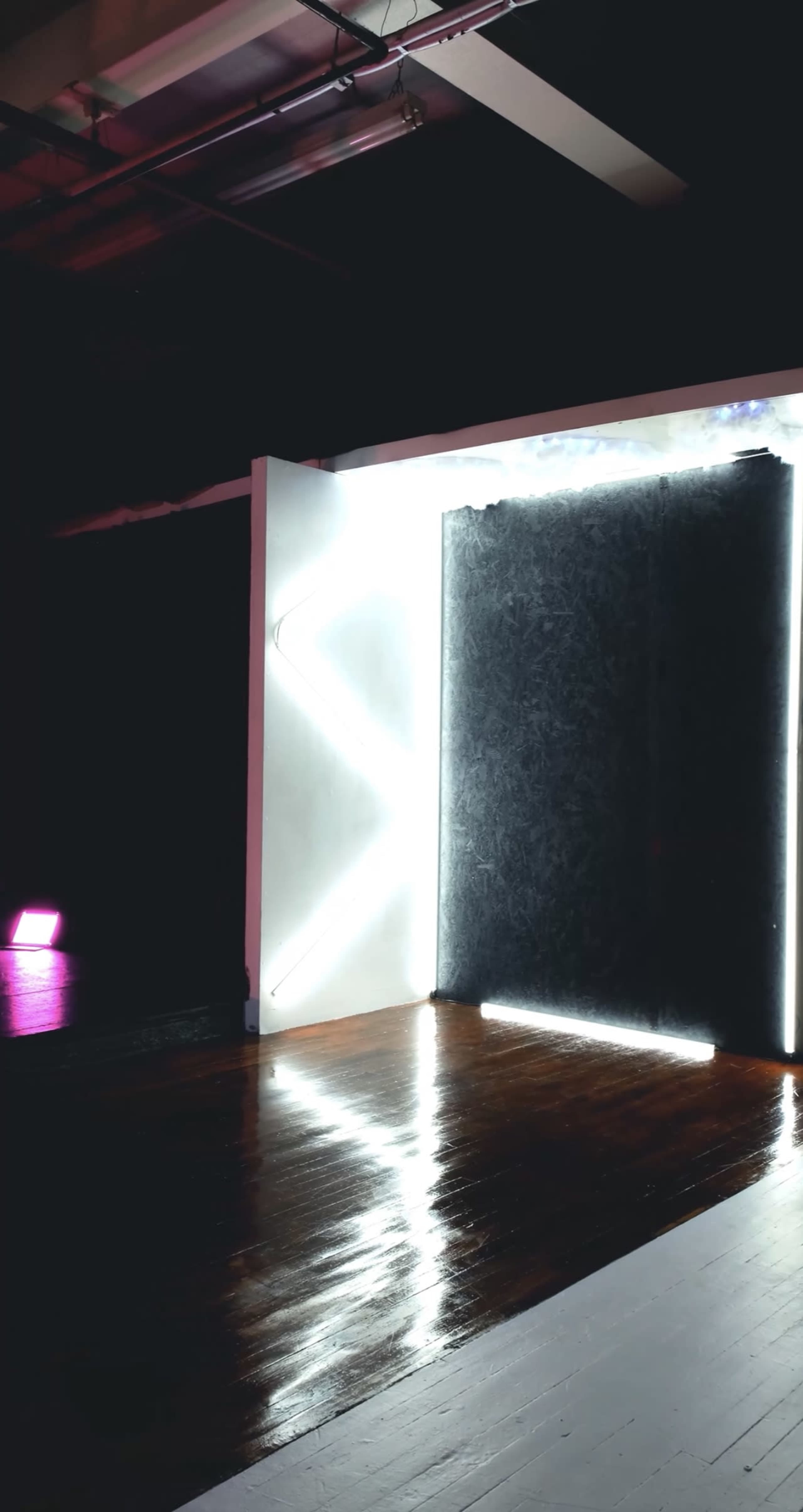 A dimly lit room featuring a wall with distinct white neon lights and a dark textured wall.