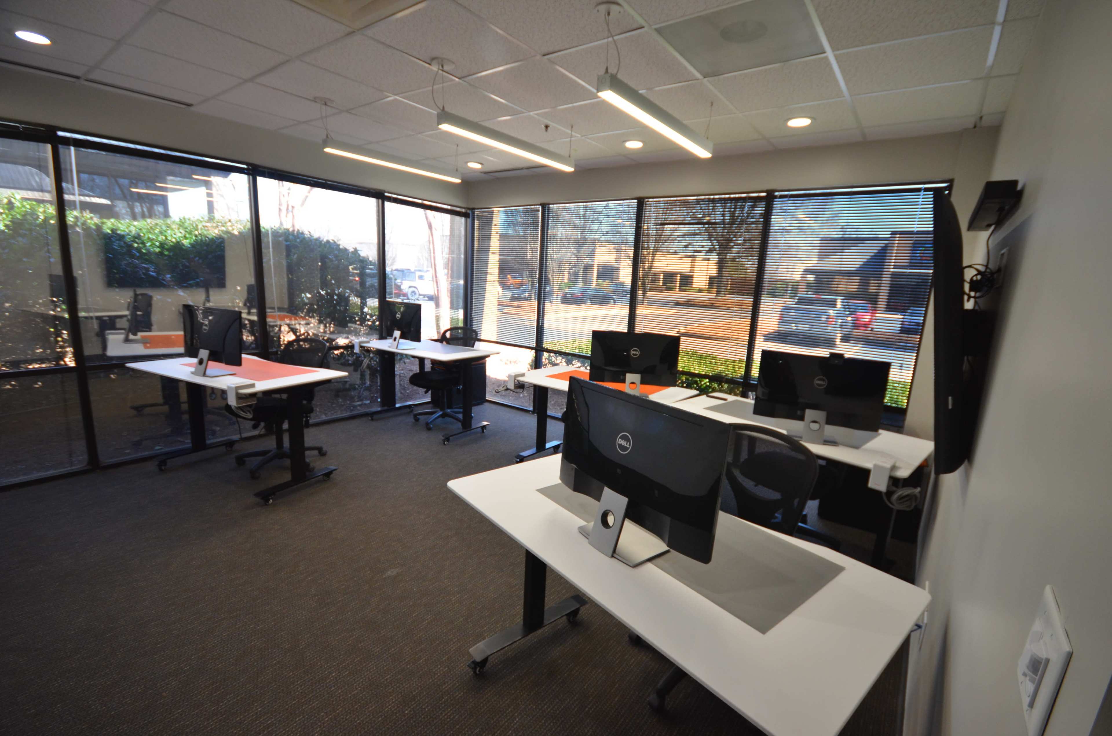 A modern office space with several desks equipped with computers and large windows allowing natural light to fill the room.