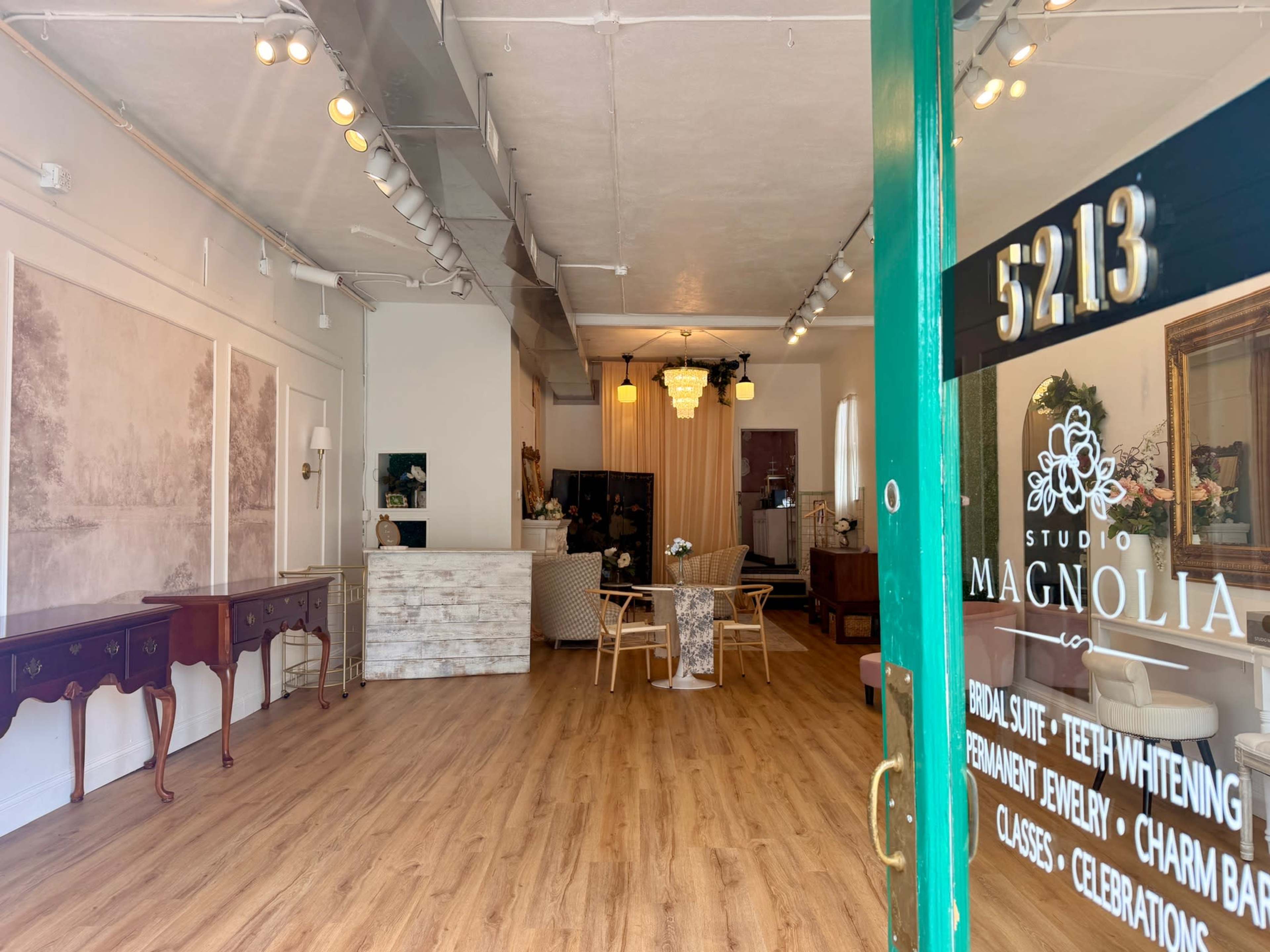 The interior of Studio Magnolia features a spacious layout with wooden flooring, contemporary furniture, and decorative accents, visible through a green entrance door with the studio's name and services listed.