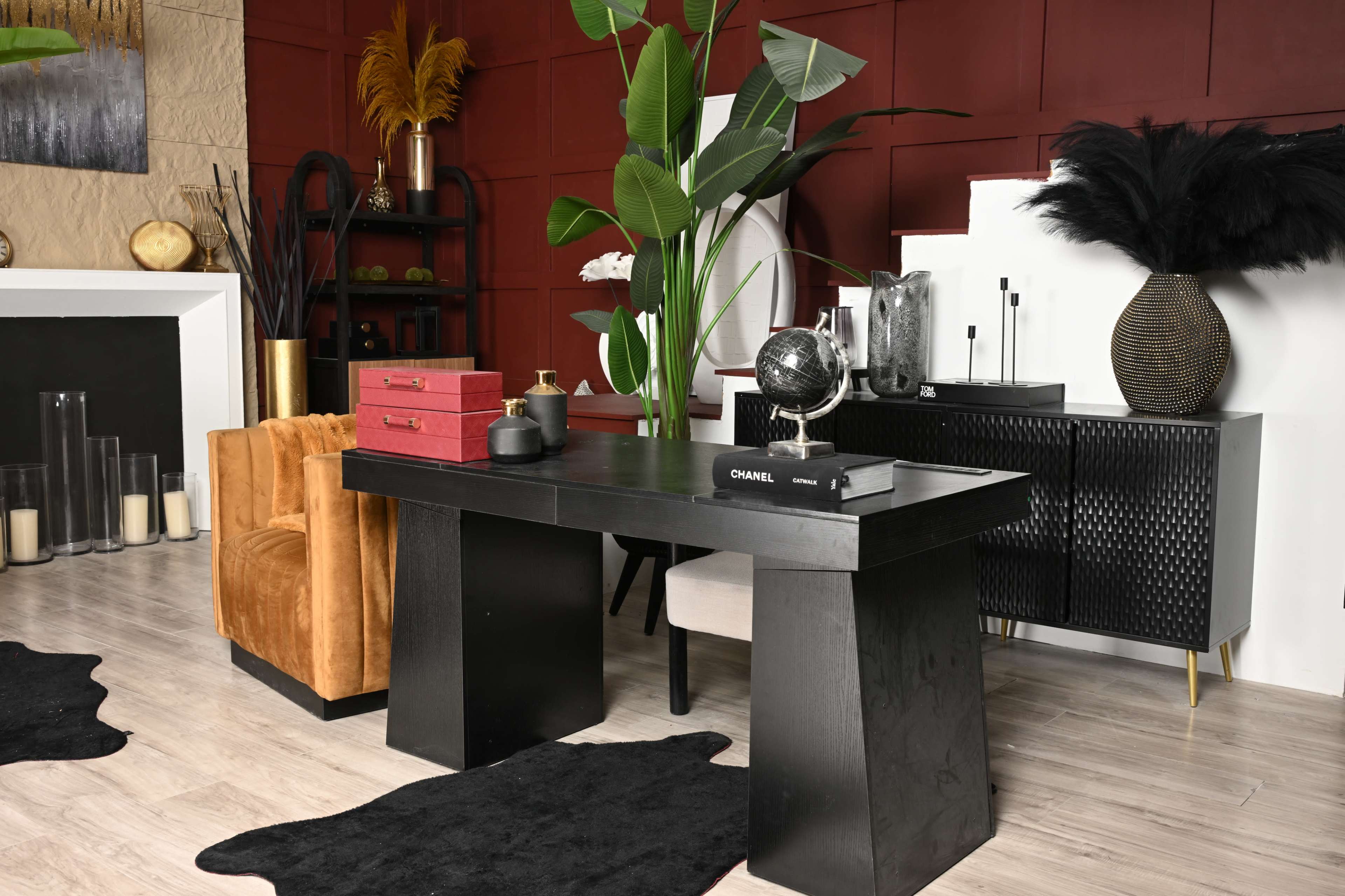 The image shows a modern interior workspace featuring a black desk, an orange chair, decorative plants, and various stylish decorative items on the desk and shelves.