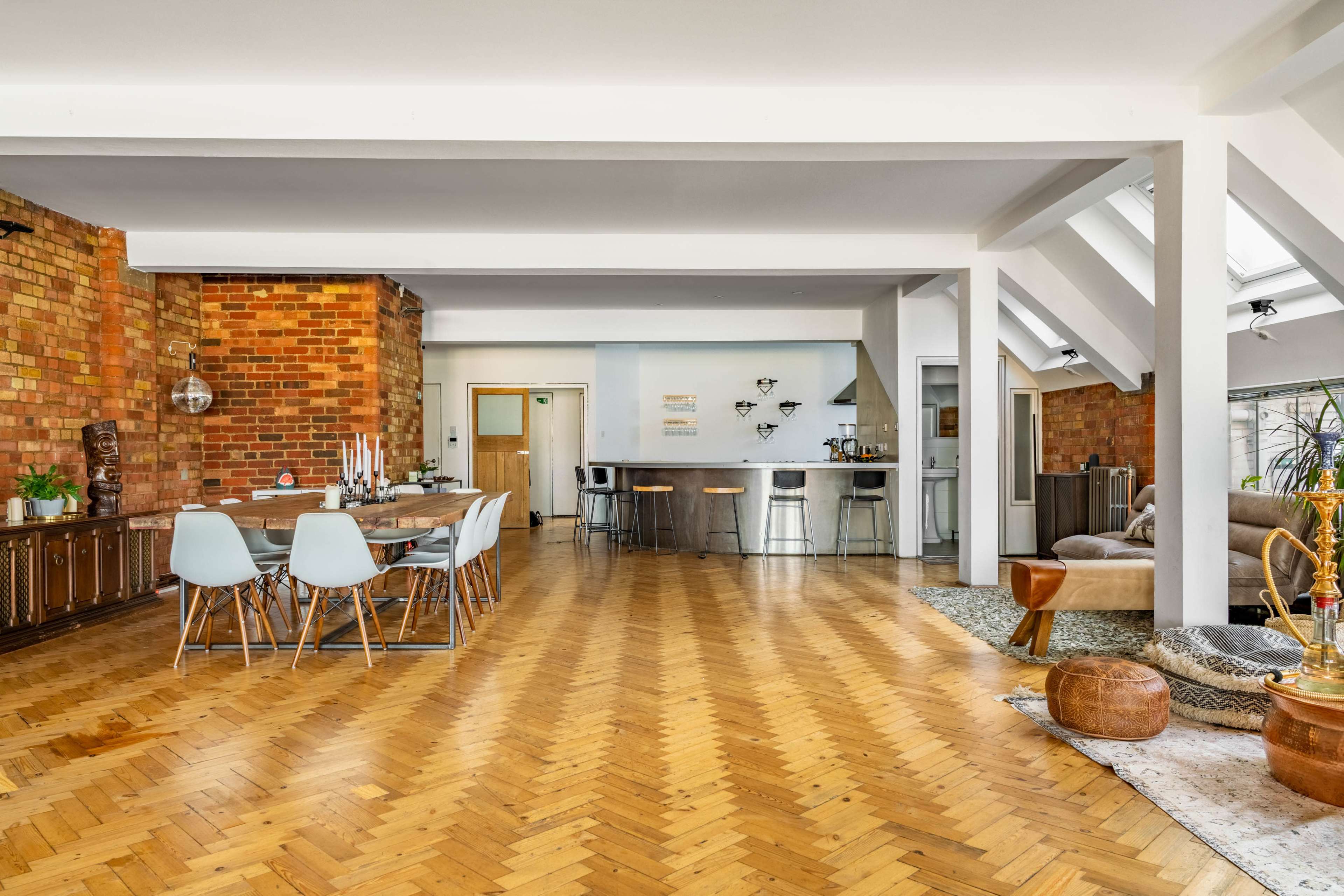 An open-concept living space featuring a dining area, a kitchen bar, and a cozy lounge with wooden flooring and brick walls.