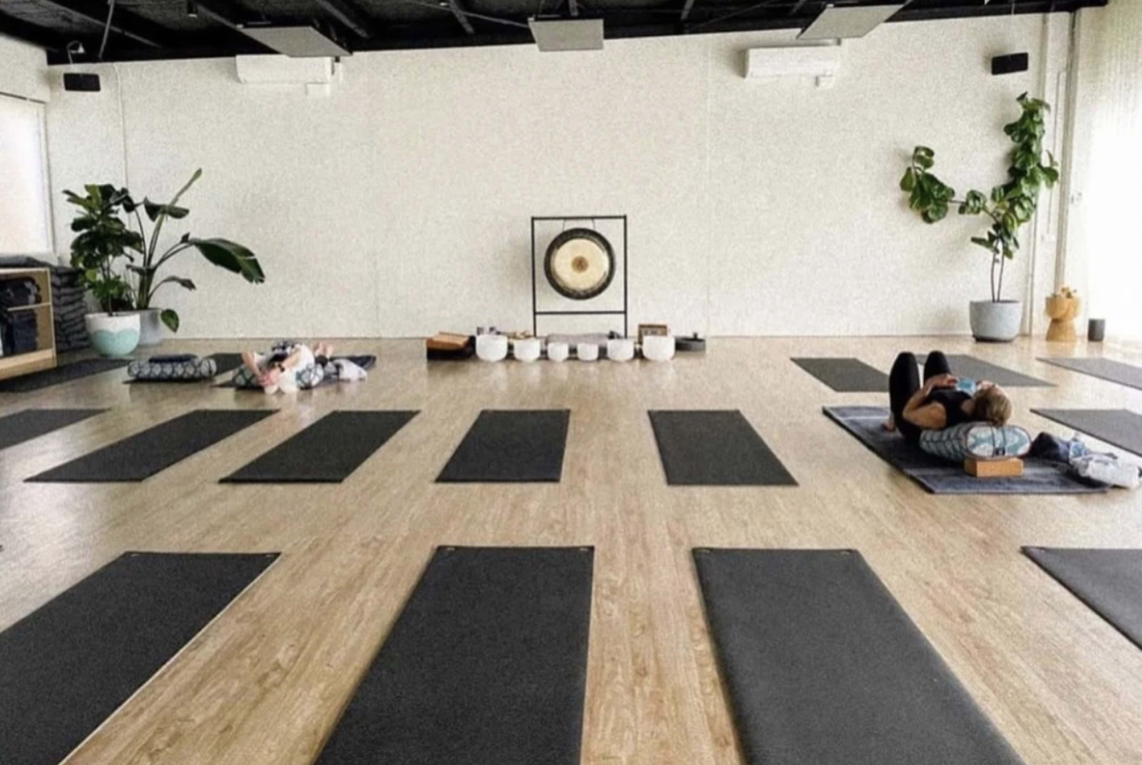 A spacious yoga studio with several exercise mats arranged on the floor, along with a gong and bowls displayed at the front.