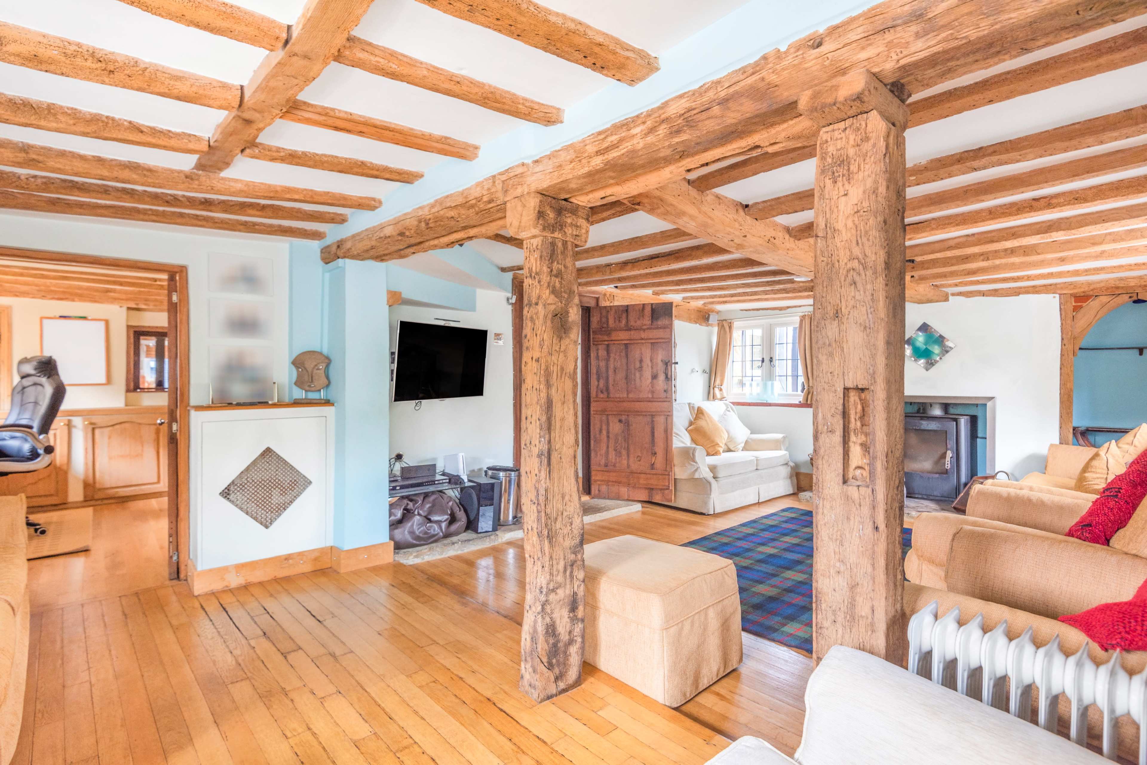 A living room with exposed wooden beams, a stone fireplace, and a mixture of upholstered furniture arranged around a rug.