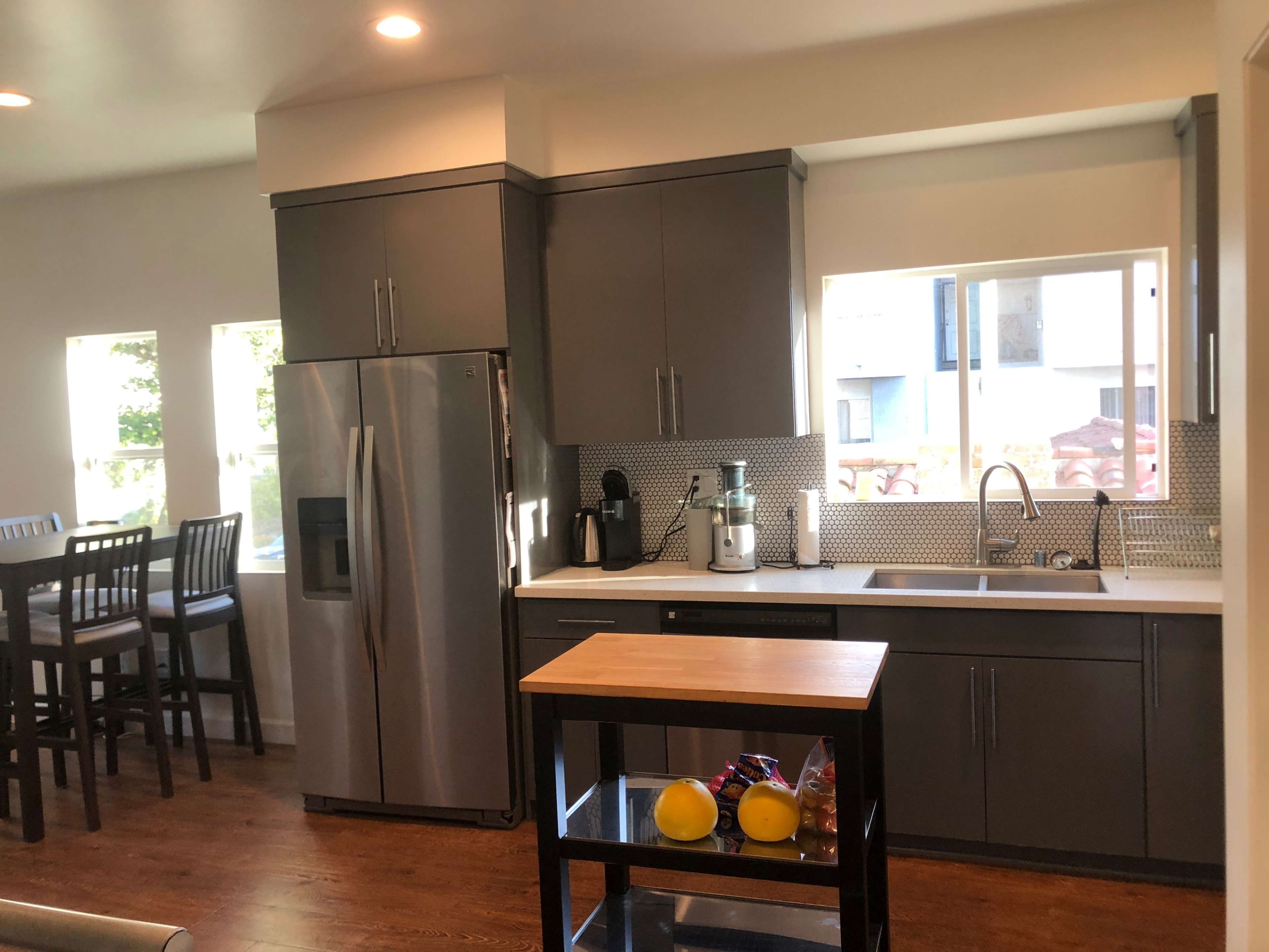 The image shows a modern kitchen with stainless steel appliances, gray cabinets, and a small island with fruit.