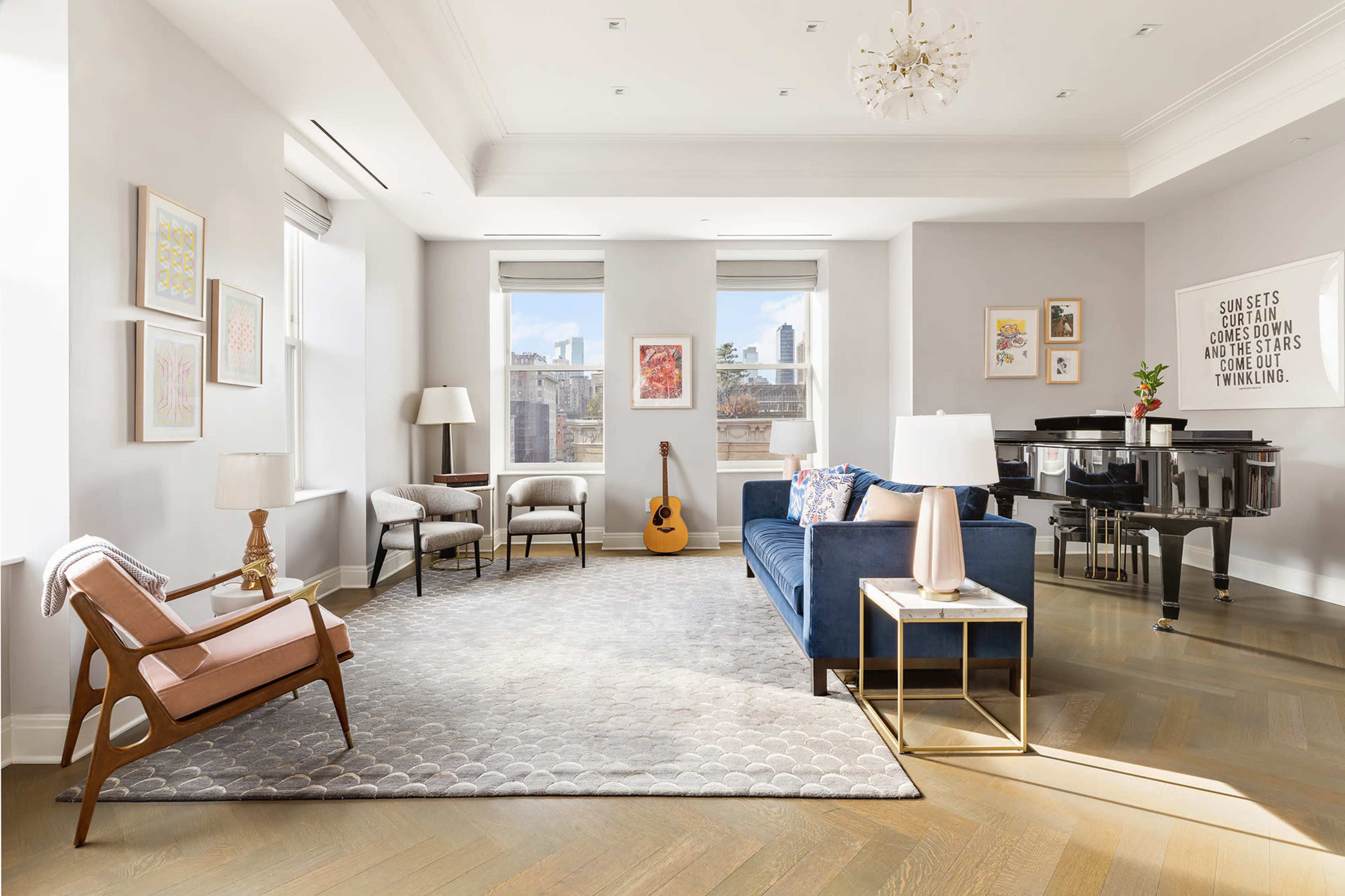 The image shows a bright living room with a blue sofa, a wooden chair, a piano, and large windows revealing a cityscape.