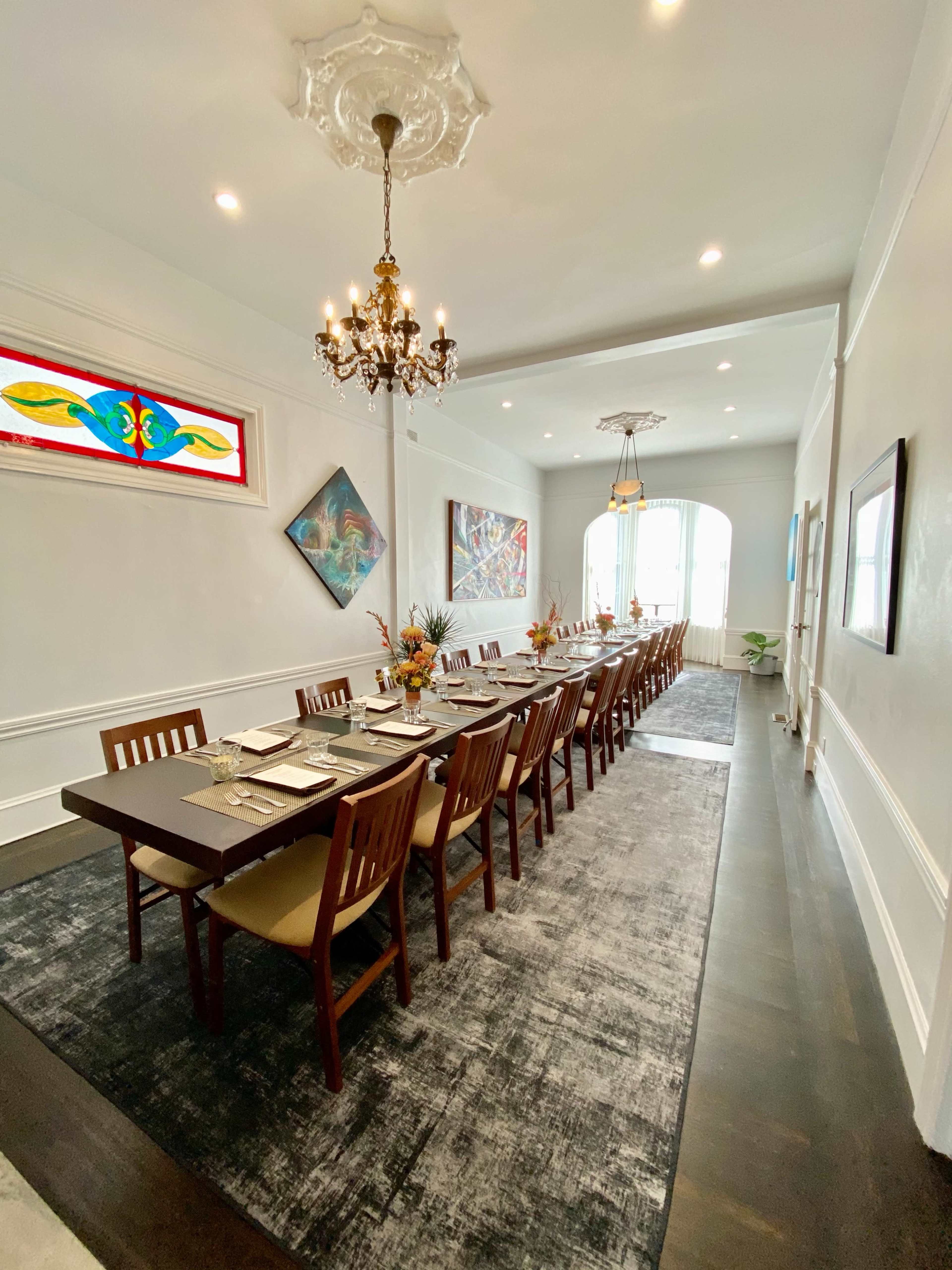 A long dining table is set in an elegantly decorated room with artistic wall pieces and a chandelier overhead.