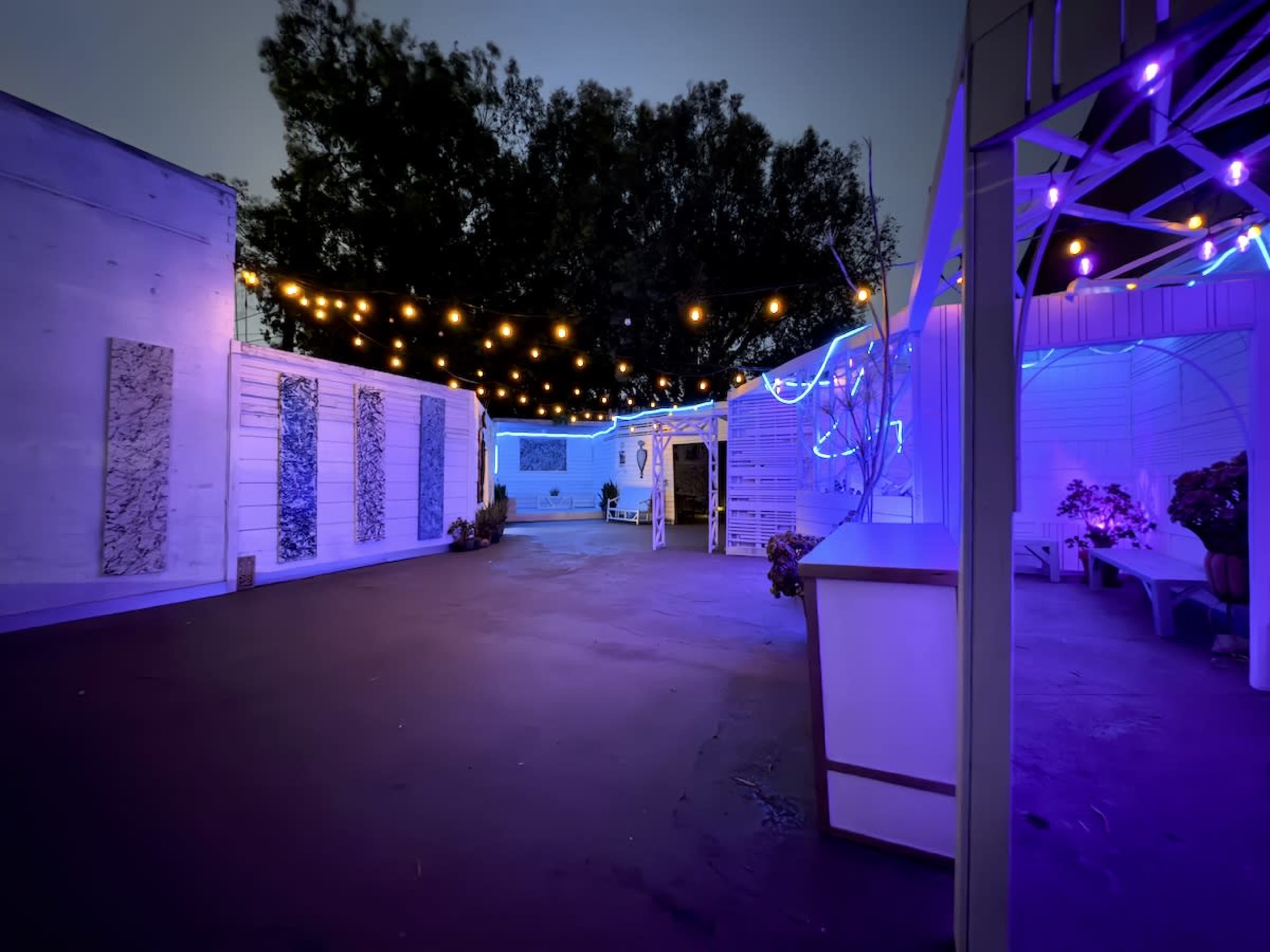 The image shows an outdoor space enclosed by walls, illuminated with colorful string lights and vibrant blue lighting.