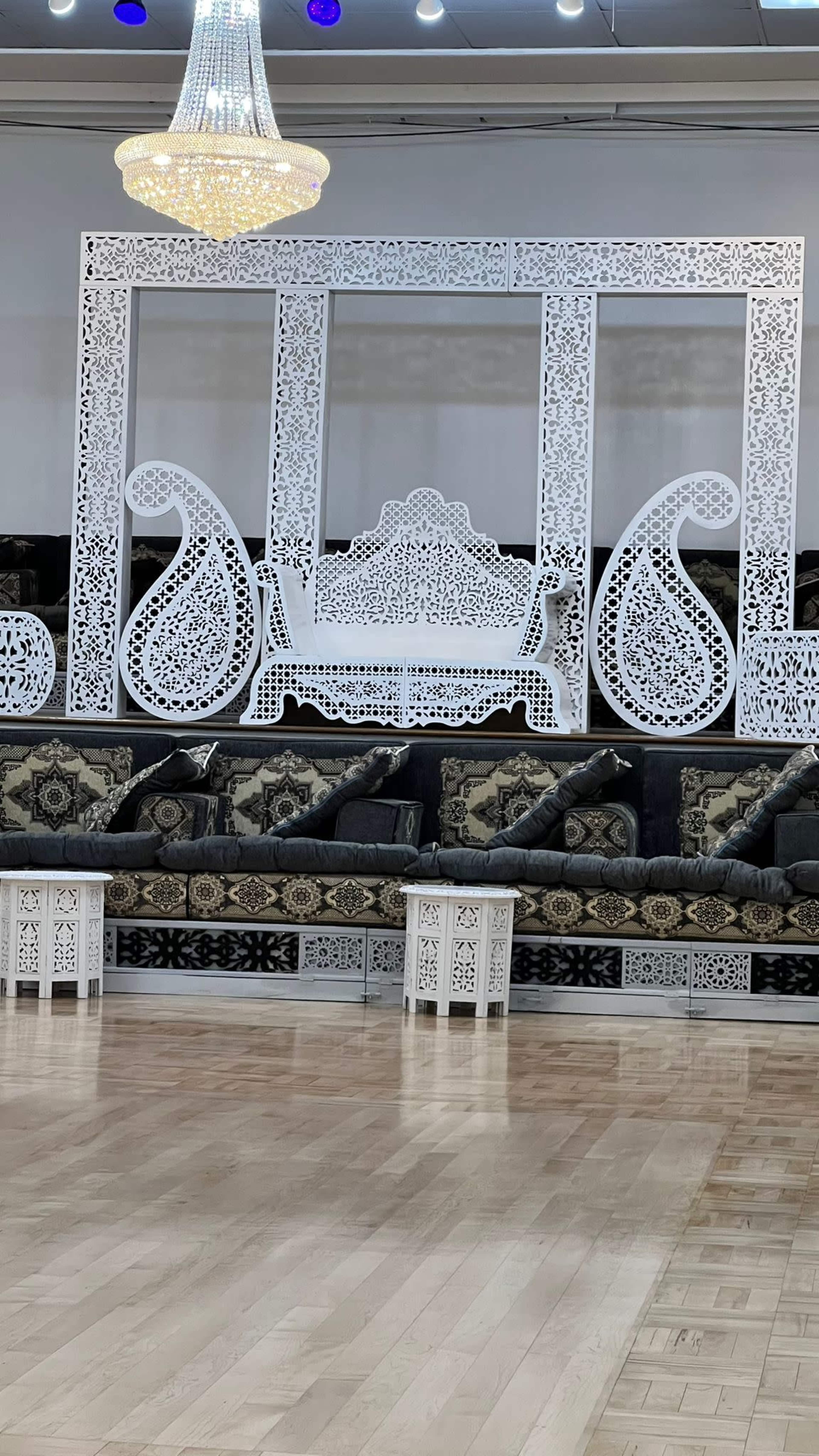 An elegantly decorated seating area featuring a white intricately carved backdrop and dark cushions on low benches.