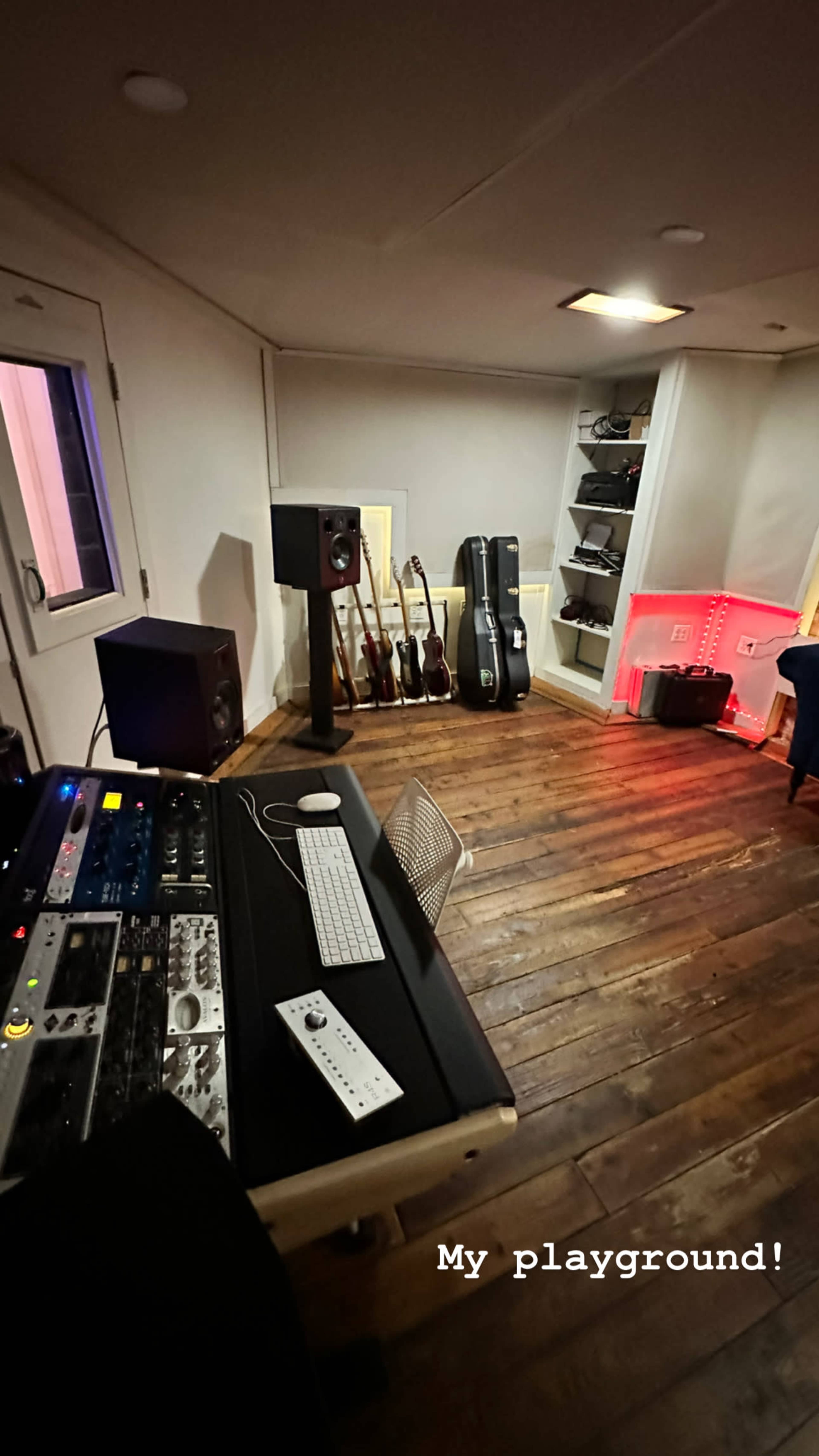 The image shows a music studio with audio equipment, instruments, and a wooden floor.