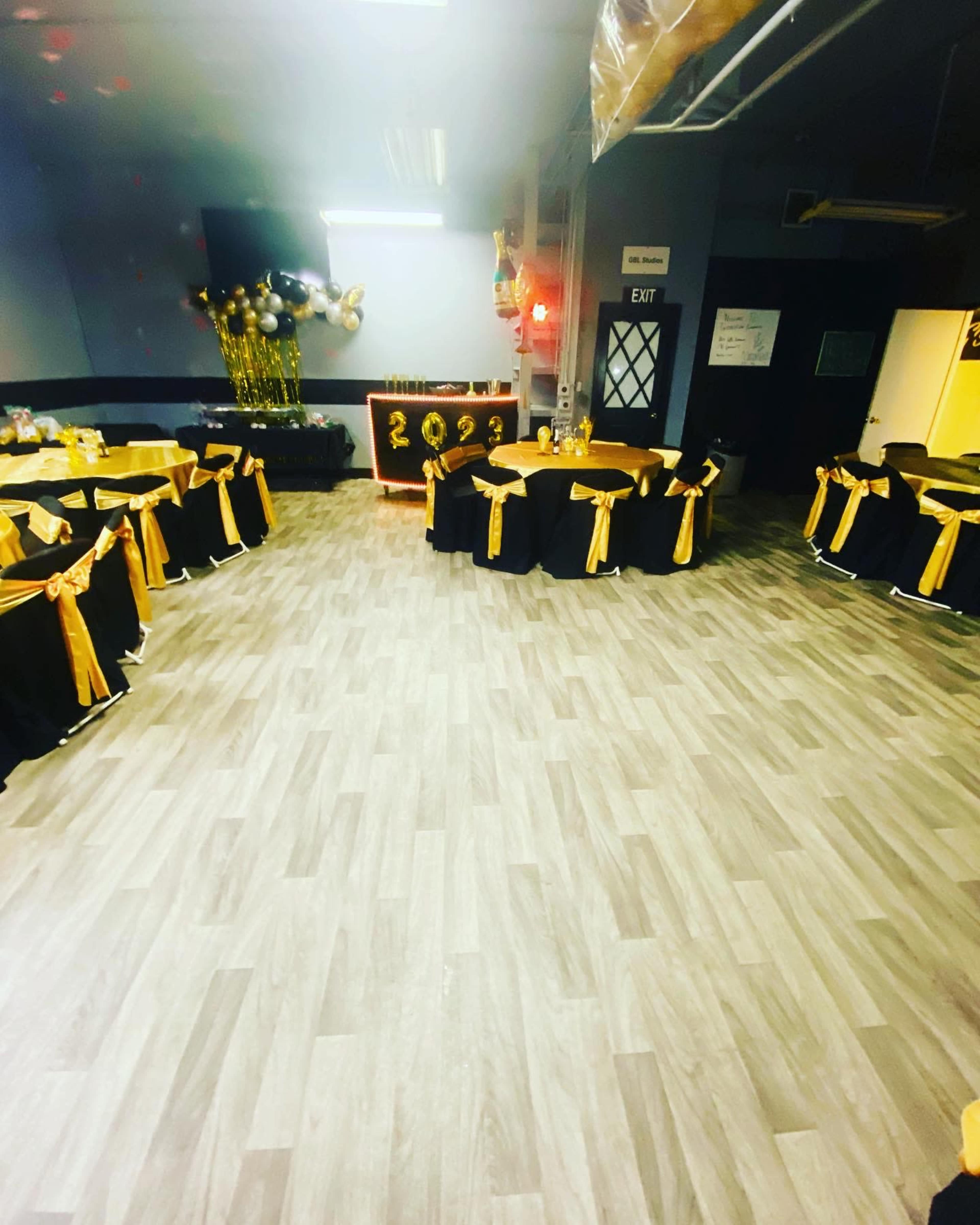 A party venue is decorated with black and gold table settings arranged in a circular layout, featuring a backdrop with the year 2023.