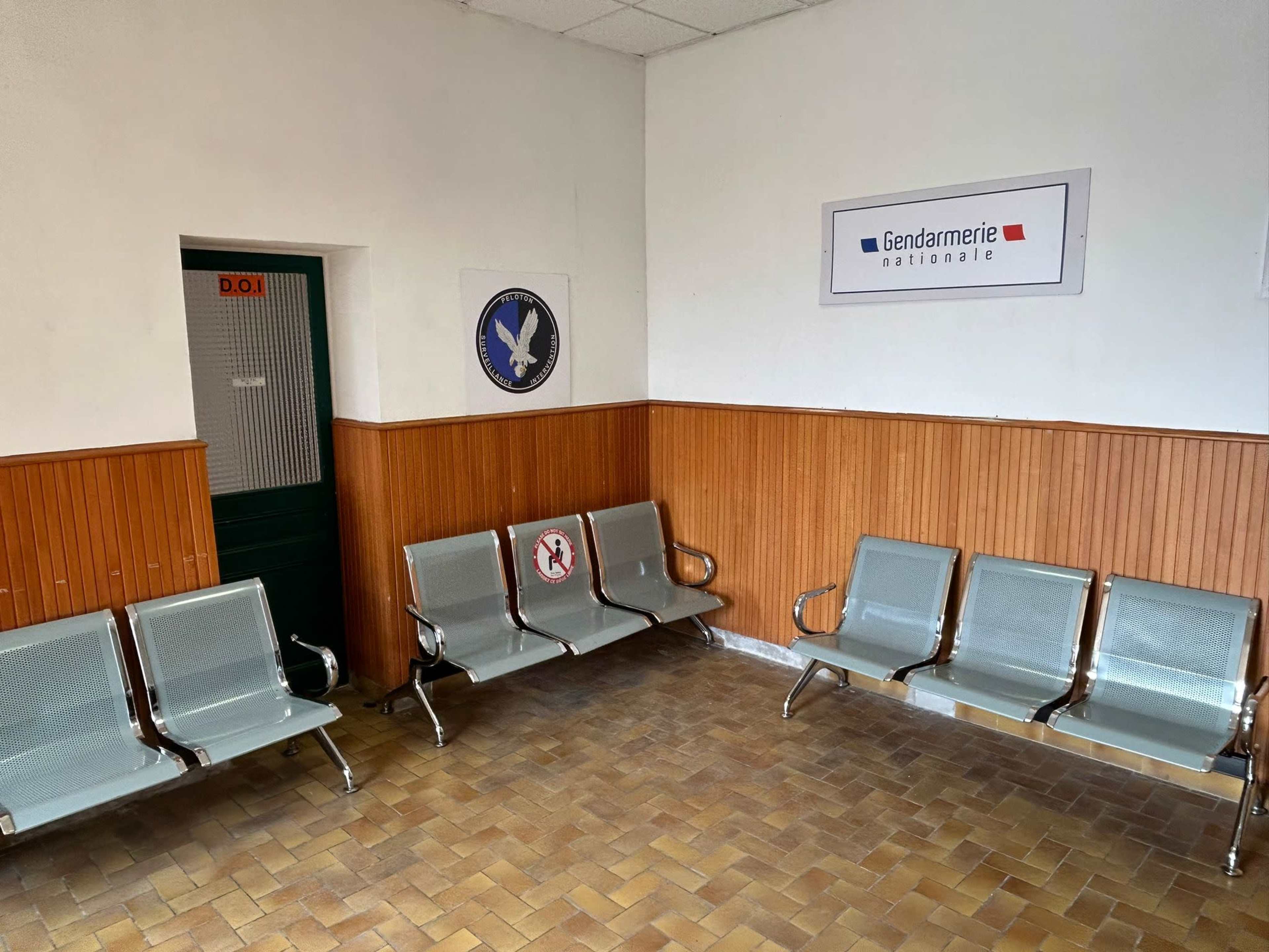 A waiting area with metallic benches and a wall displaying signs for the national gendarmerie.