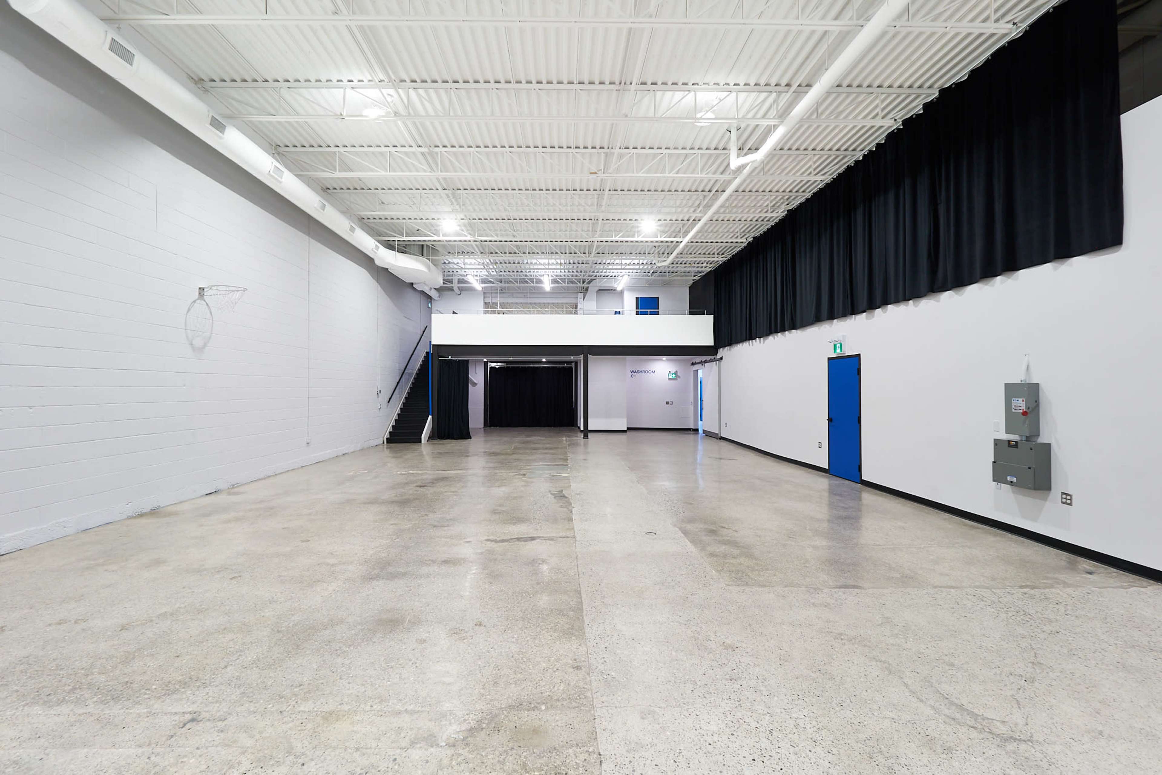 A spacious, empty hall with a polished concrete floor, white walls, and black drapes at one end.