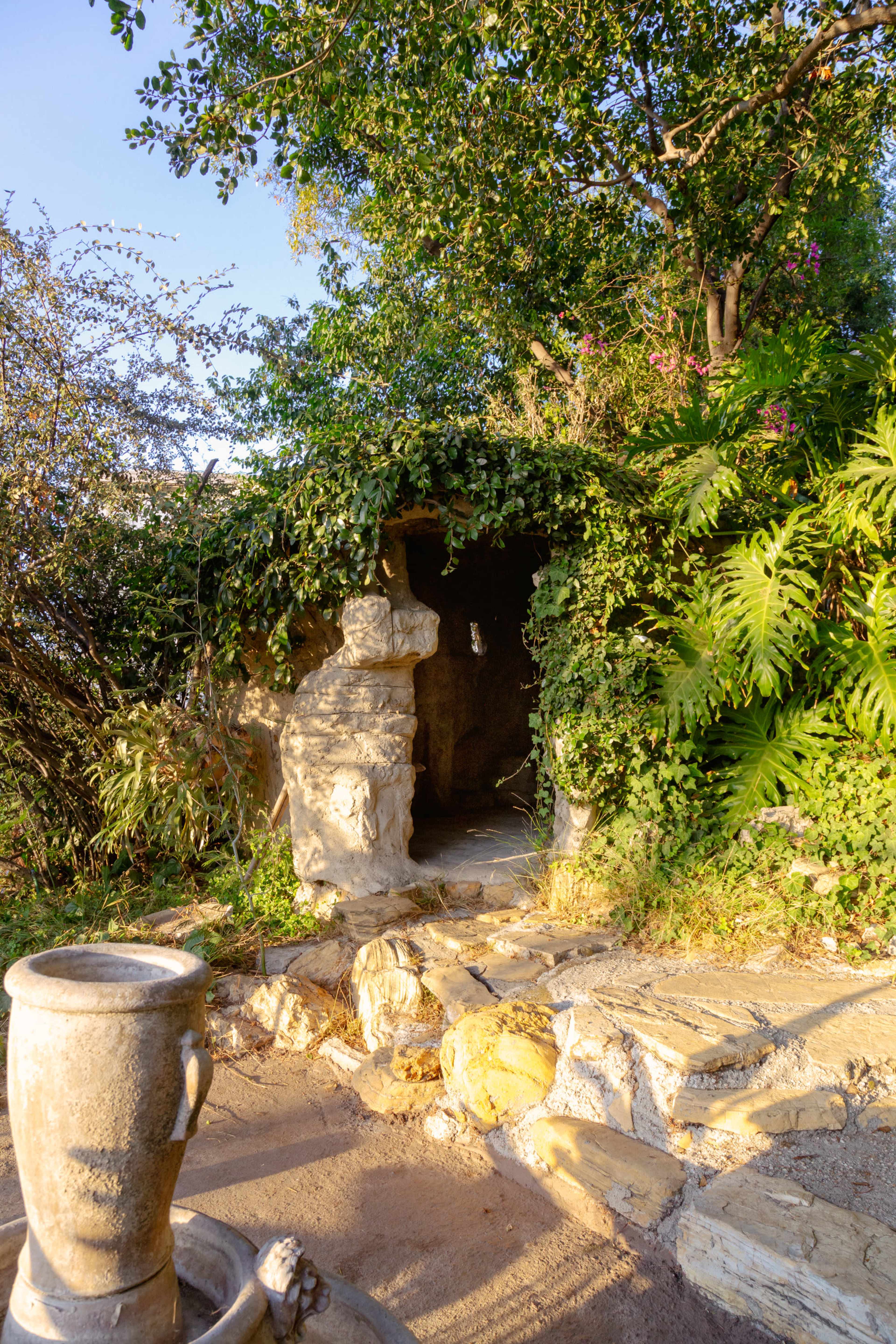 A stone pathway leading to a cave-like entrance surrounded by lush greenery and vibrant plants.
