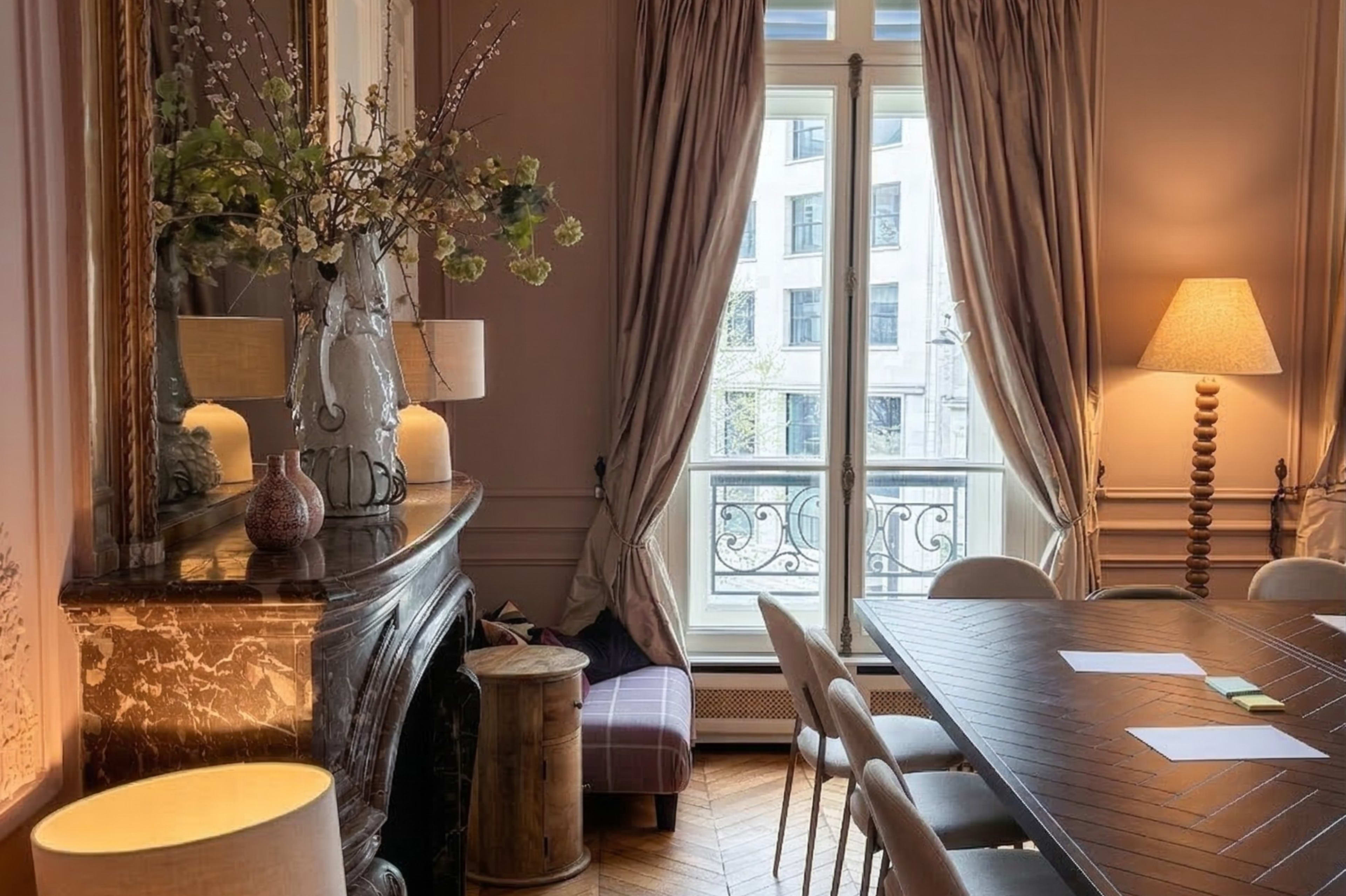 The image shows a well-decorated meeting room with a large wooden table, elegant curtains, and a decorative fireplace.