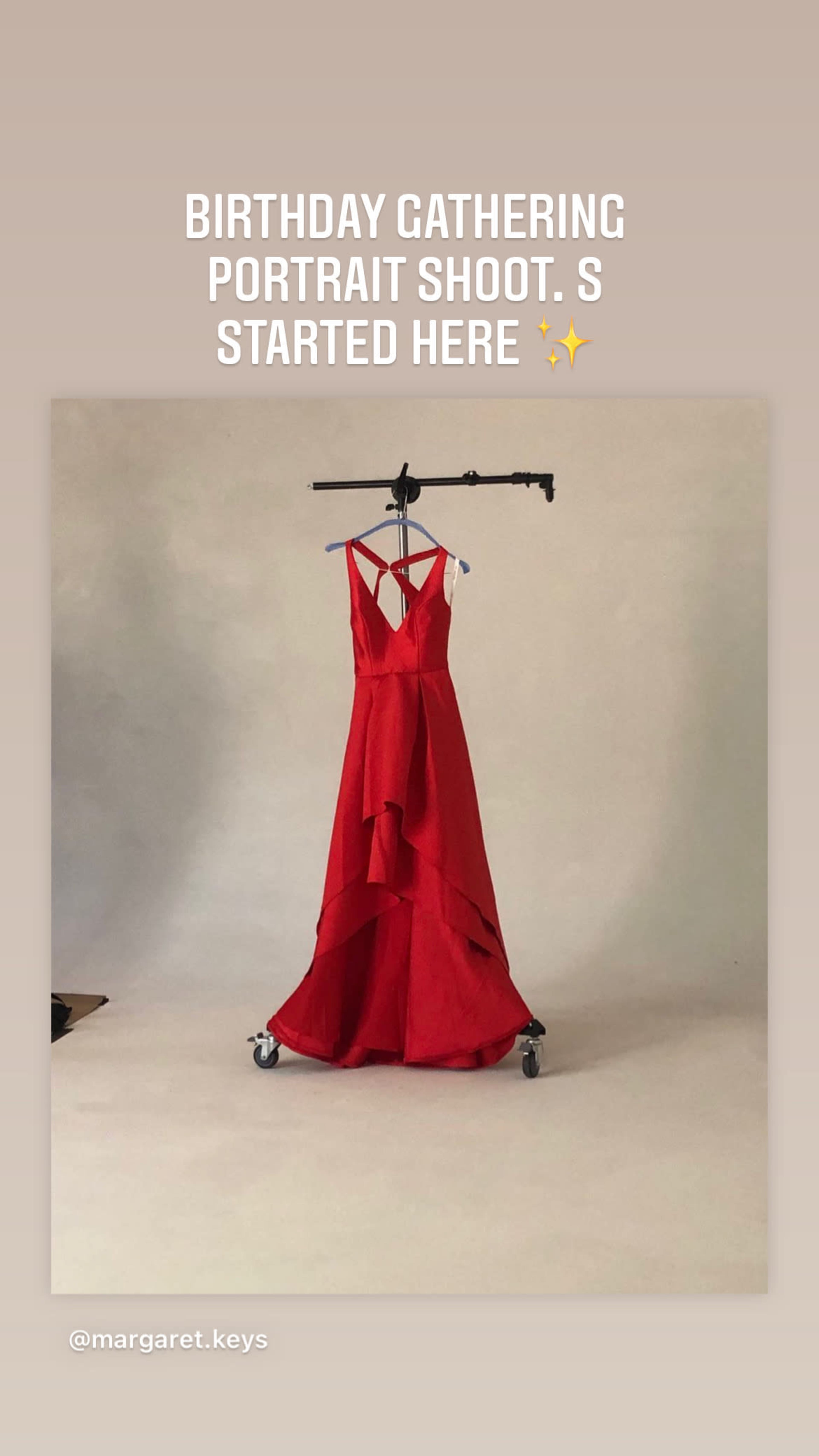 A red dress is hung on a clothing rack against a plain backdrop in a portrait studio setting.