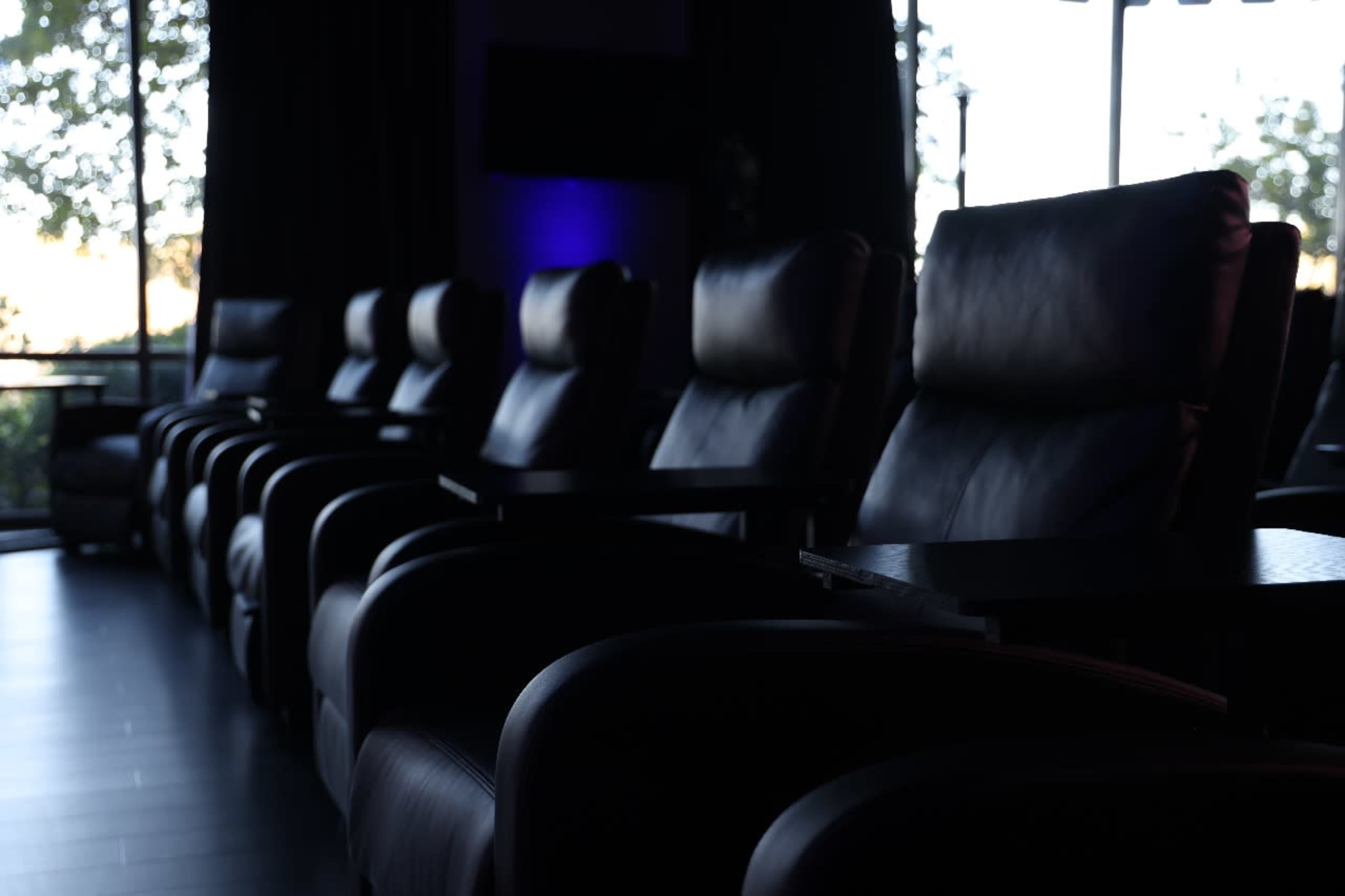 The image shows a row of black leather reclining chairs with small side tables in a dimly lit room.