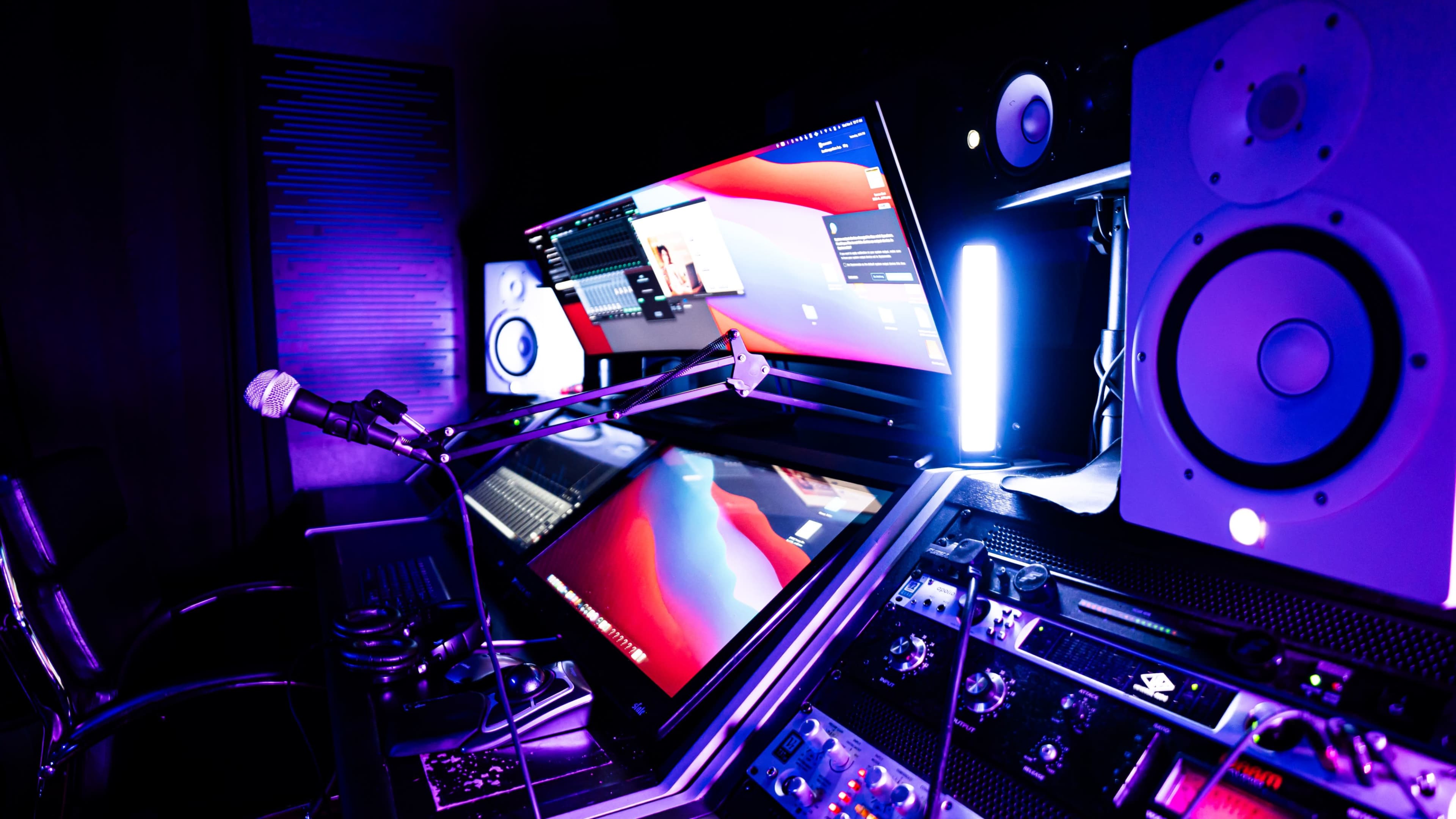 A modern audio recording studio setup with a large screen, studio monitors, and a microphone positioned on a desk.