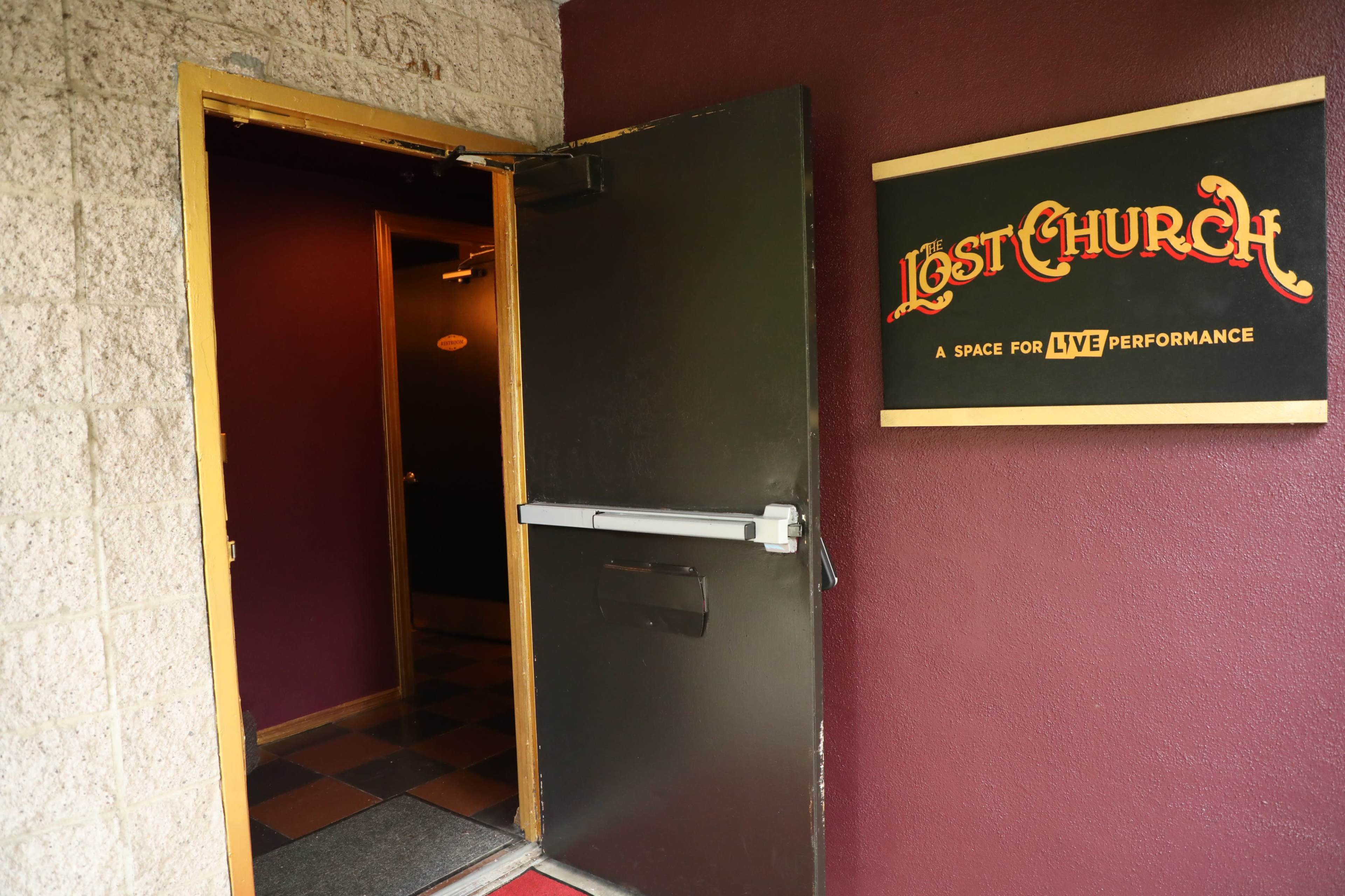 The image shows an open doorway leading to a venue called "Lost Church," which is designated for live performances, with a maroon wall and a sign beside the entrance.