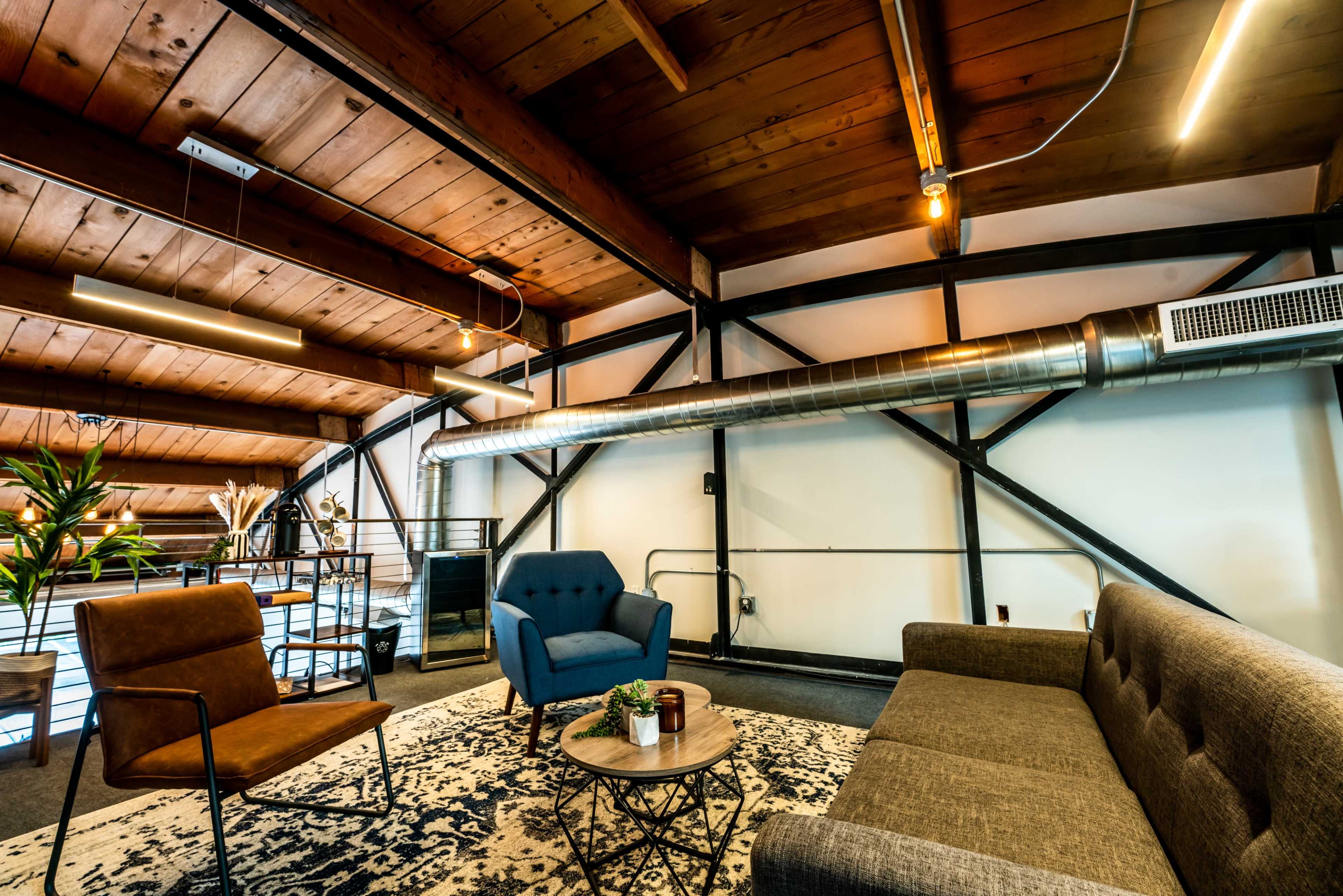 A modern living space with a wooden ceiling, a gray sofa, a blue armchair, and a small coffee table on a patterned rug.