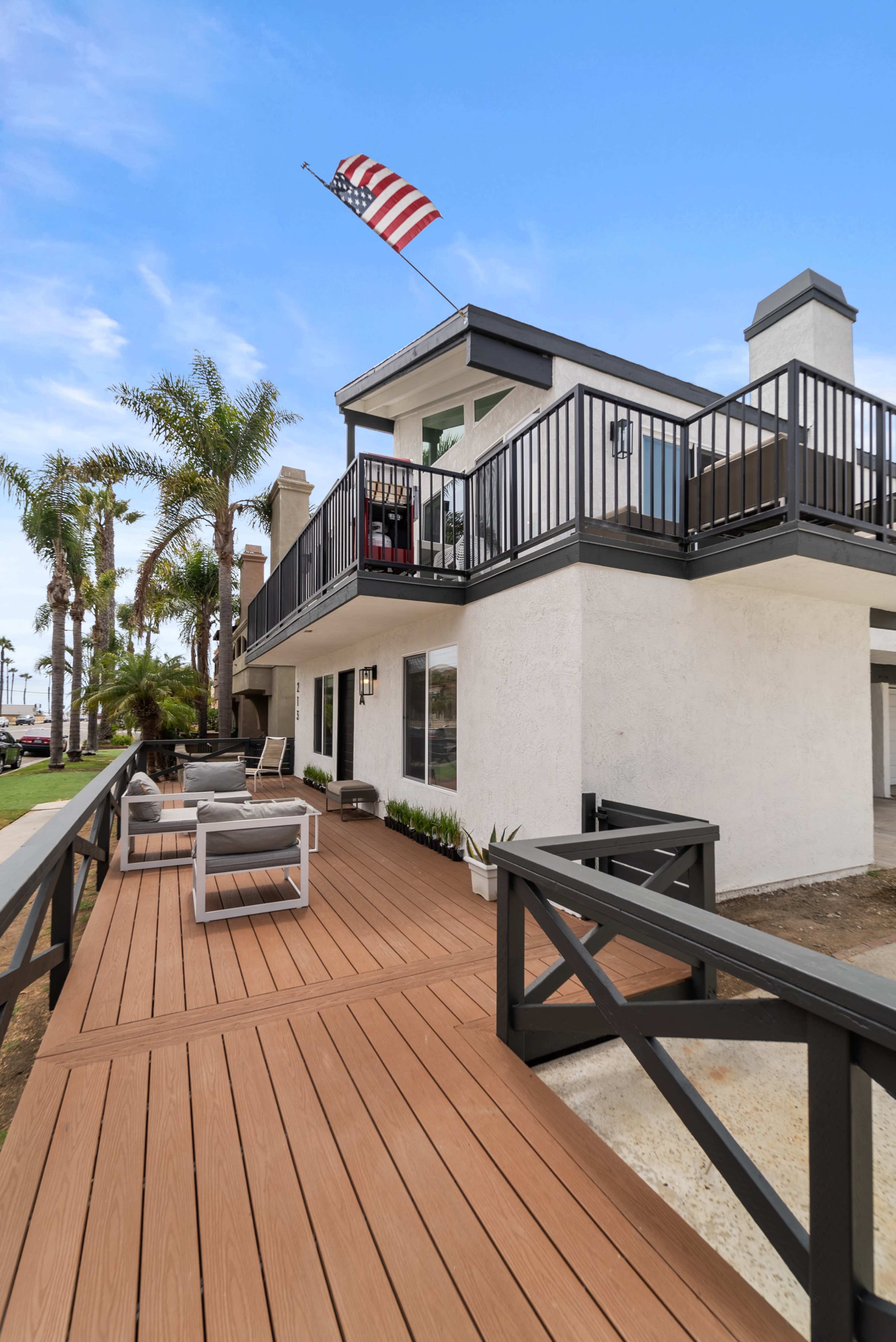 A two-story white house with a balcony, palm trees nearby, and an American flag flying above.