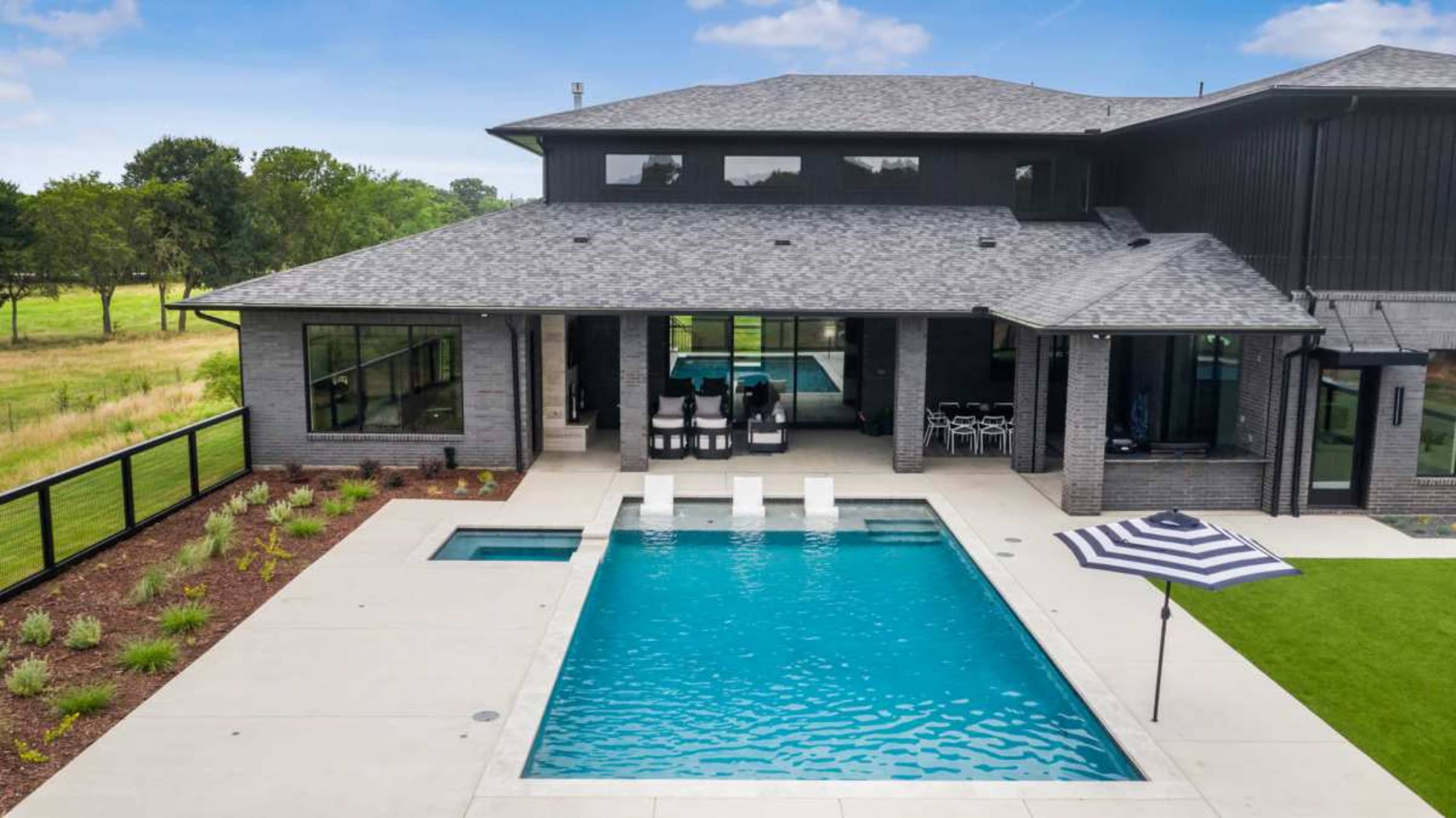 A modern house featuring a rectangular swimming pool surrounded by a patio and landscaped greenery.