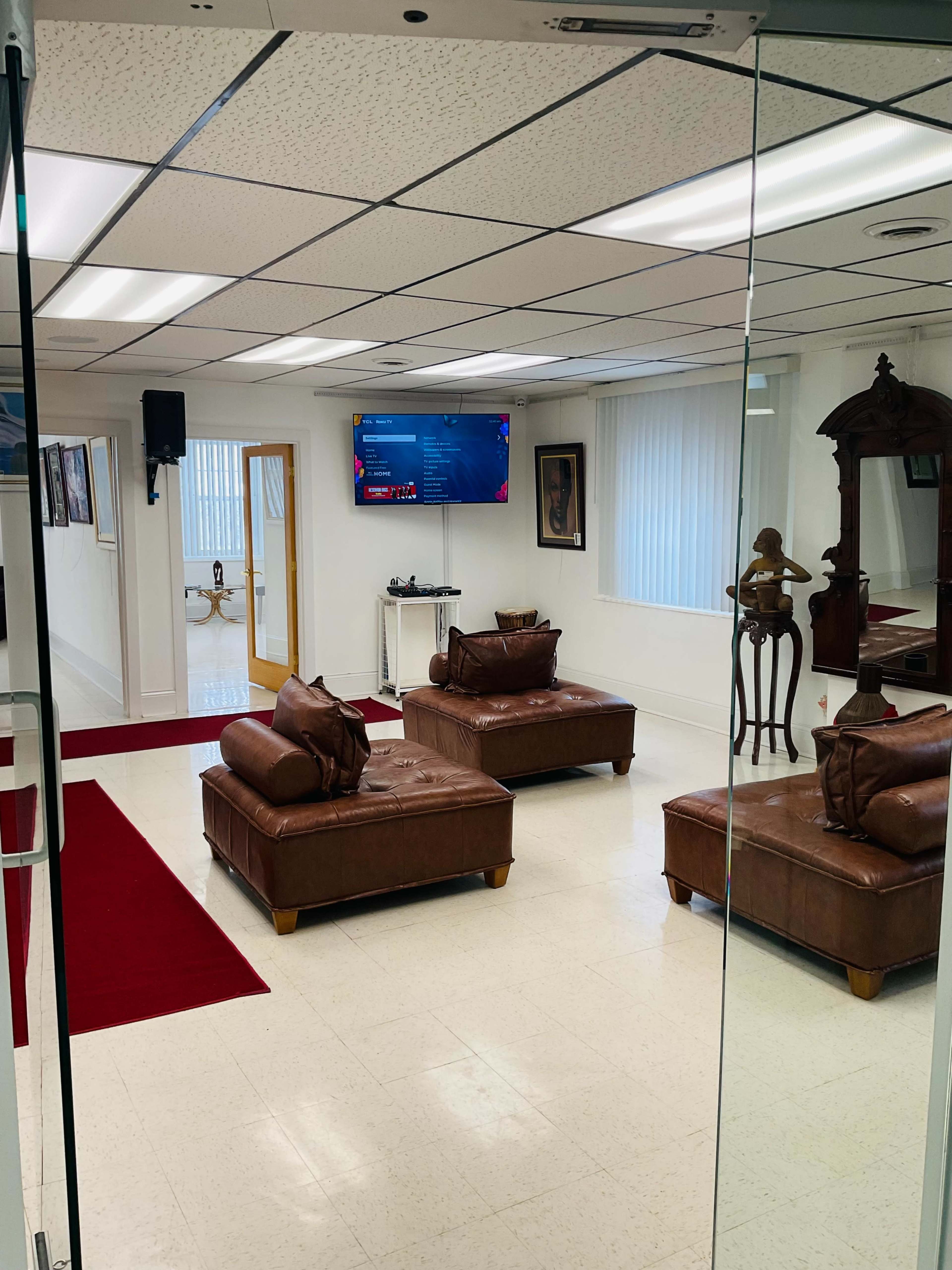 A bright room with two brown leather sofas, a large wall-mounted television, and light-colored walls adorned with framed artwork.