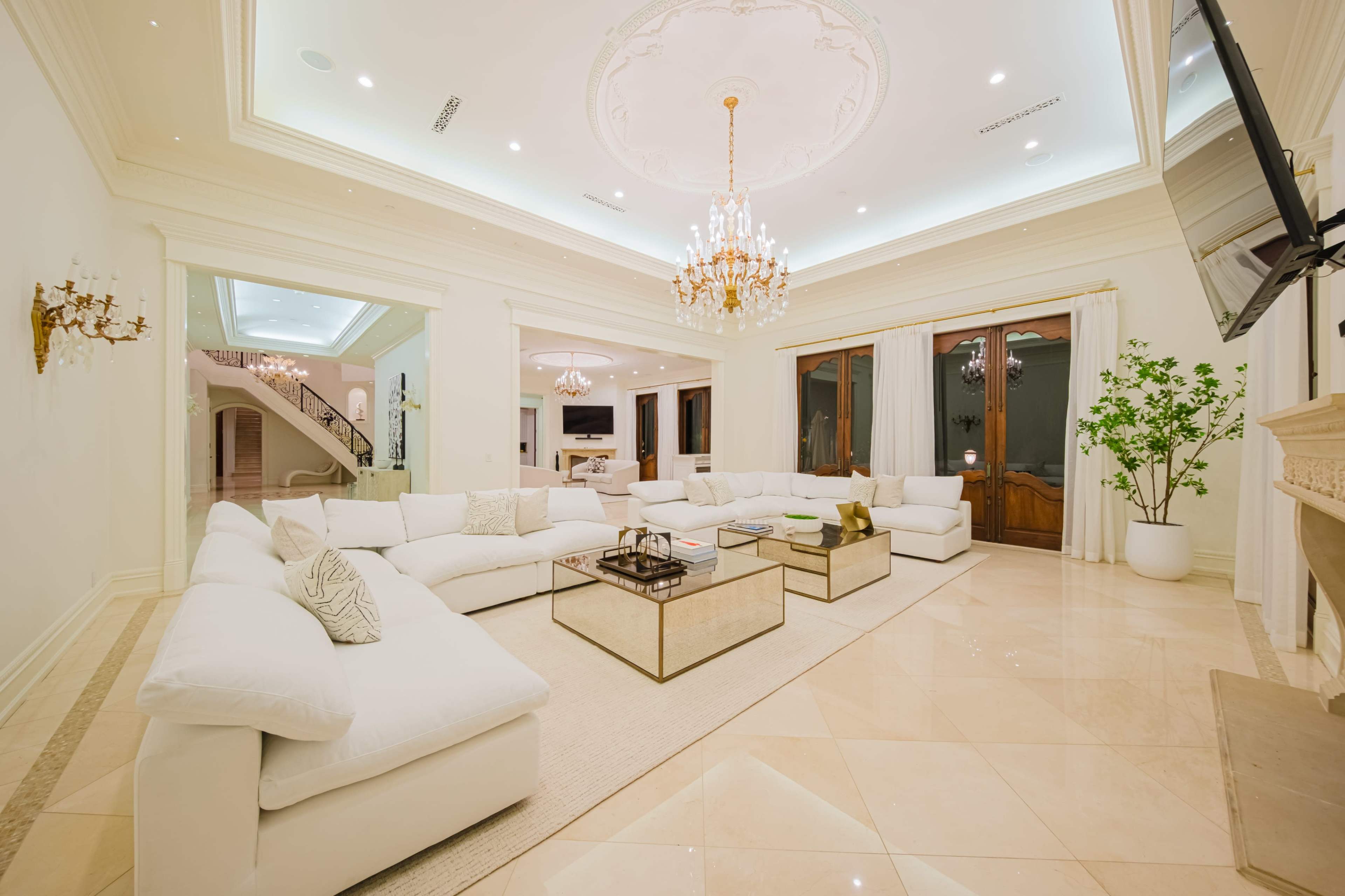 The image shows a spacious living room with a white sectional sofa, a glass coffee table, and elegant lighting fixtures.