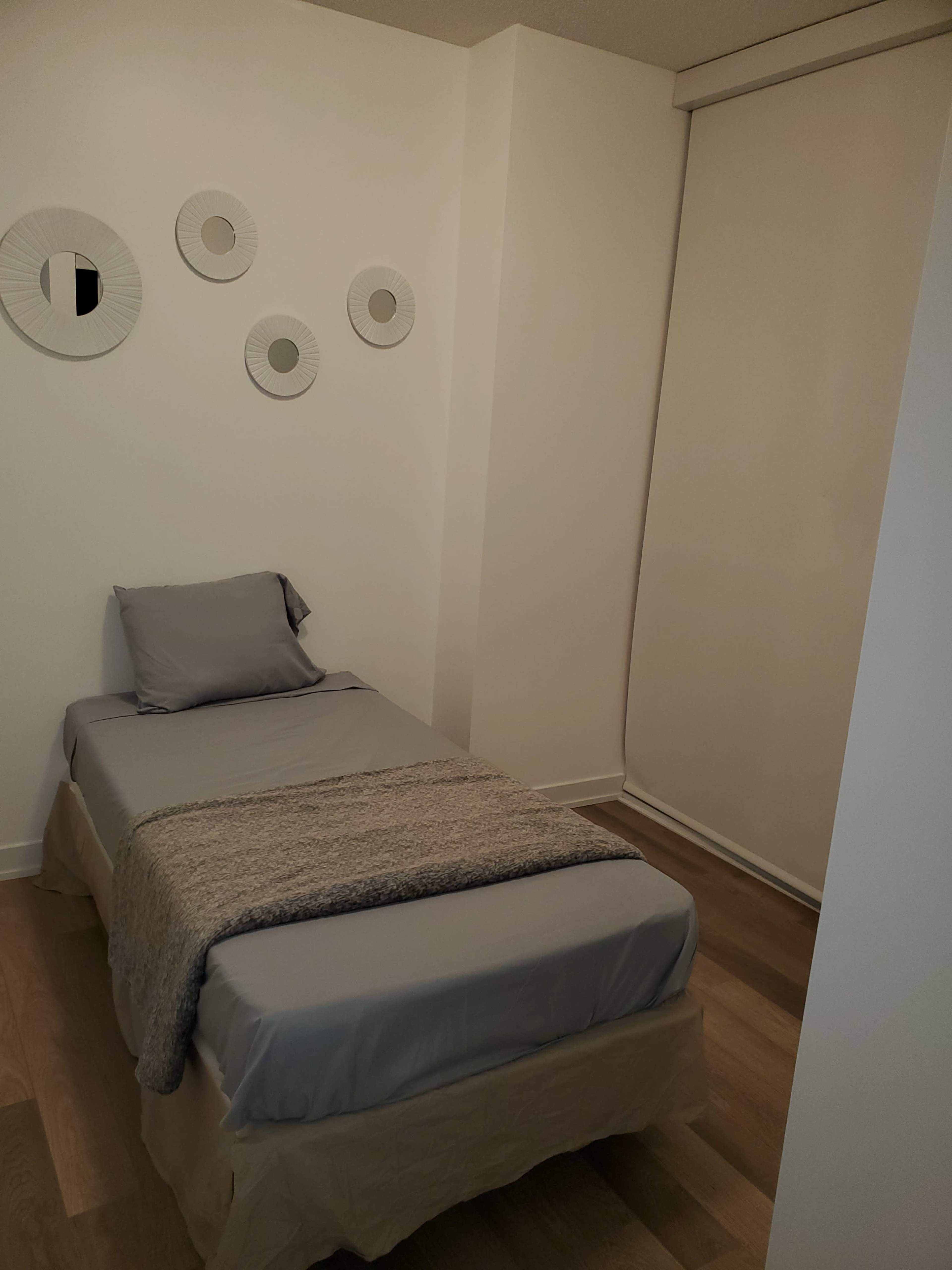 A small bedroom with a single bed, a gray blanket, and circular wall decor.