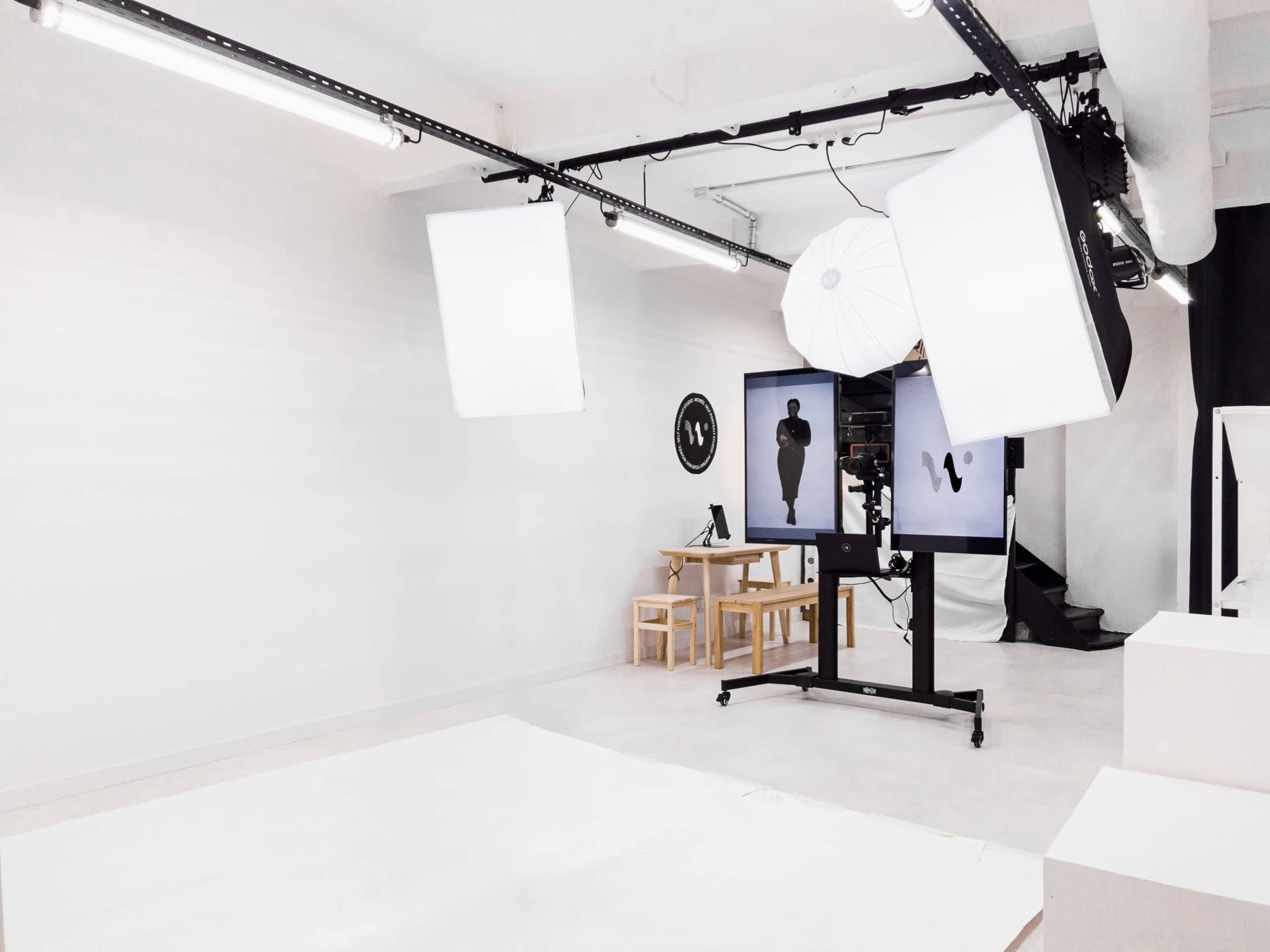 A photography studio features large softbox lights, a backdrop, and a minimalist set with a small table and chairs.