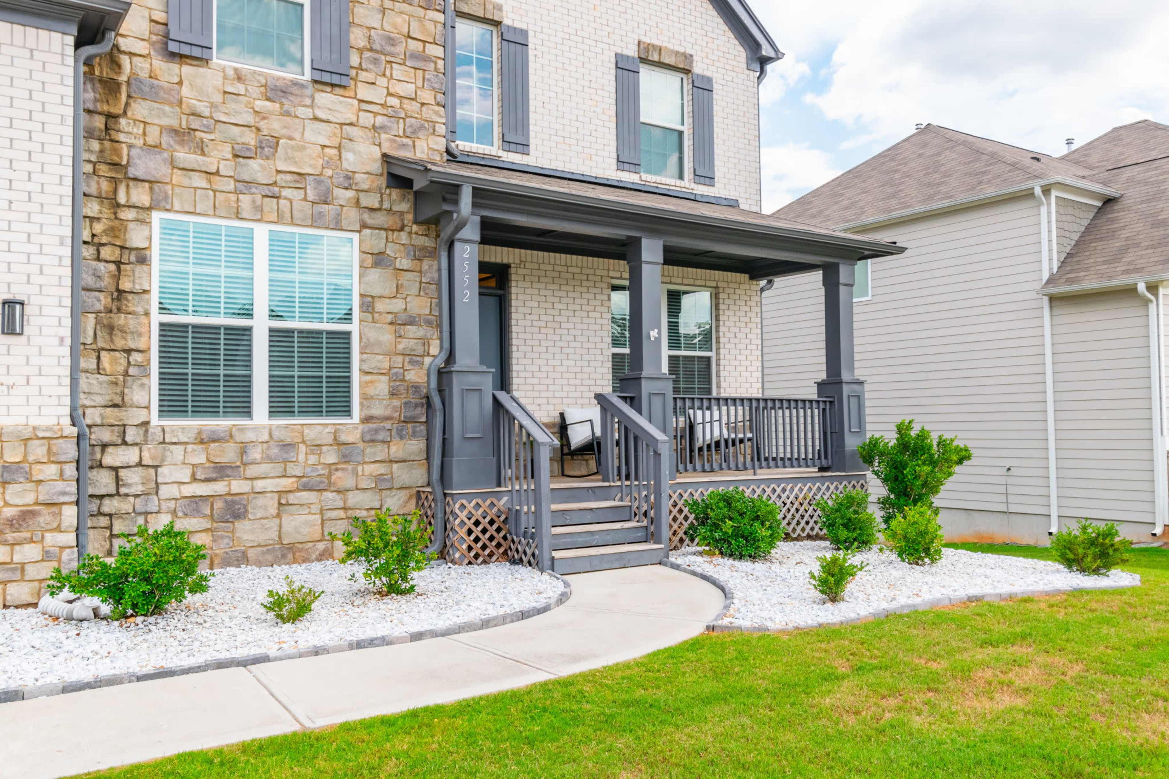 A two-story house with a stone and brick facade features a front porch and landscaped yard.