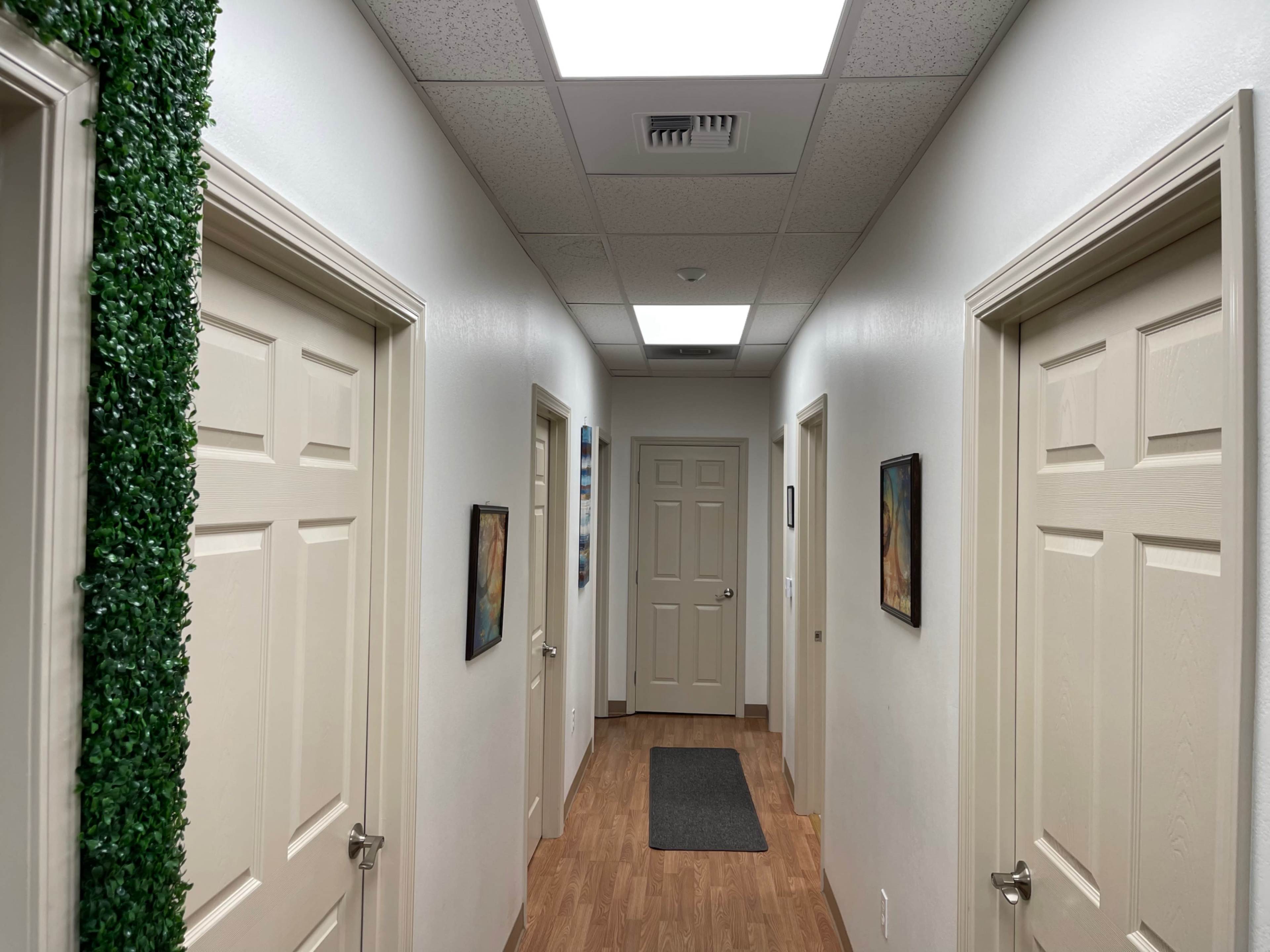 A narrow hallway features several closed doors on either side, with wall-mounted artworks and a green wall accent.