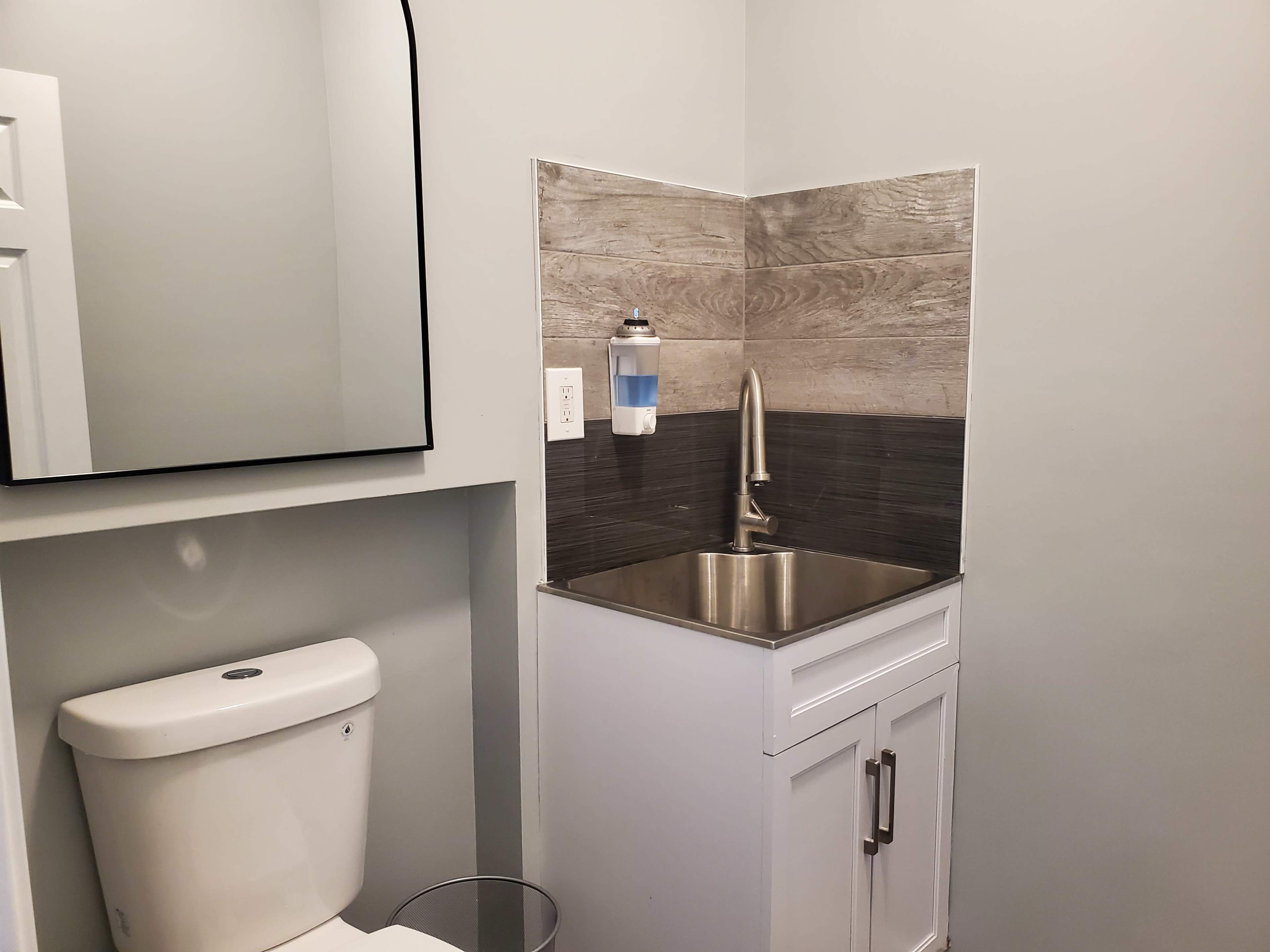 The image shows a compact bathroom featuring a toilet beside a small sink with a sleek faucet and an upper mirror.