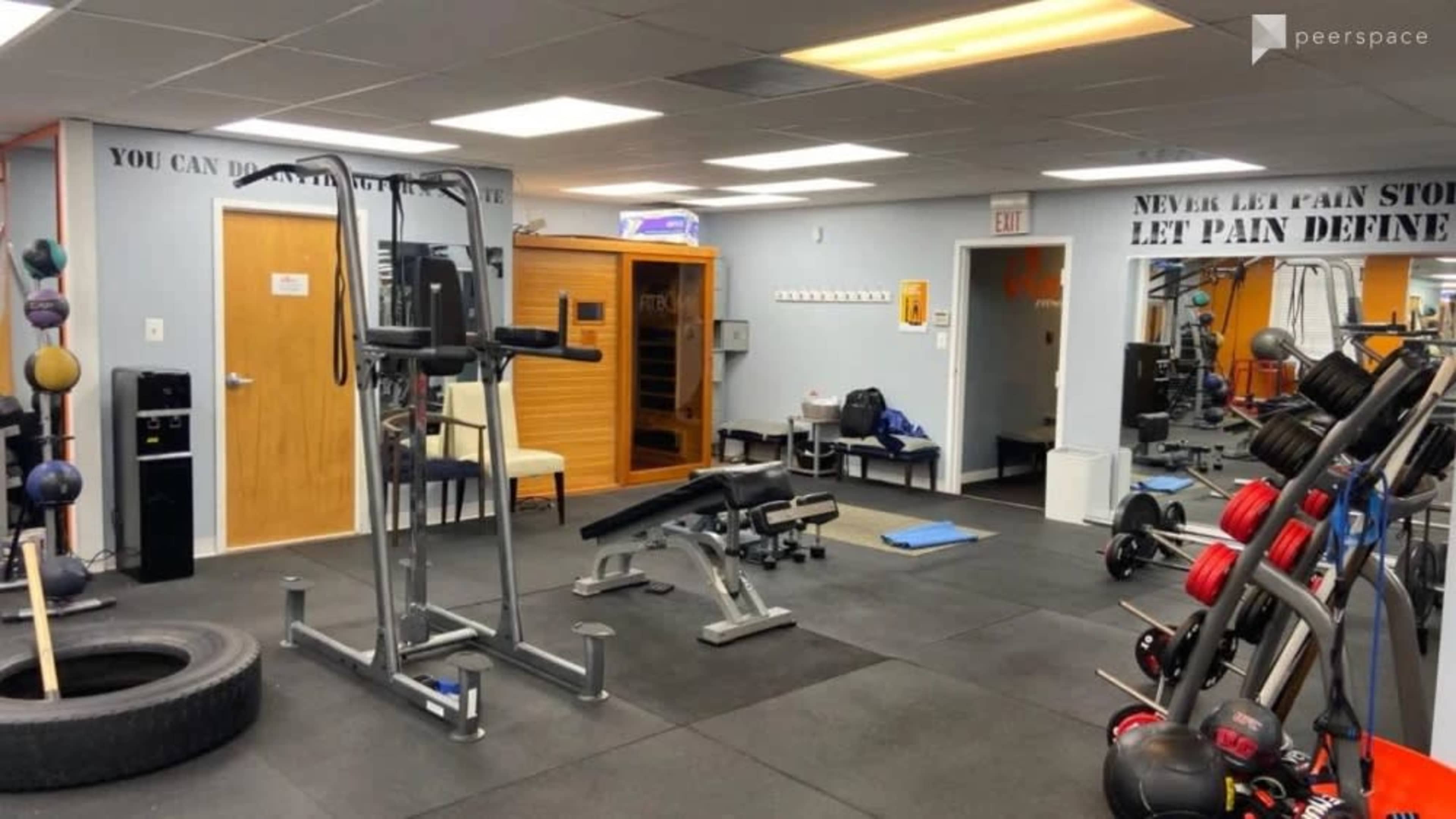 A fitness gym with various exercise equipment, including weights, a bench, and a multi-station machine, situated in a room with gray walls and wood accents.