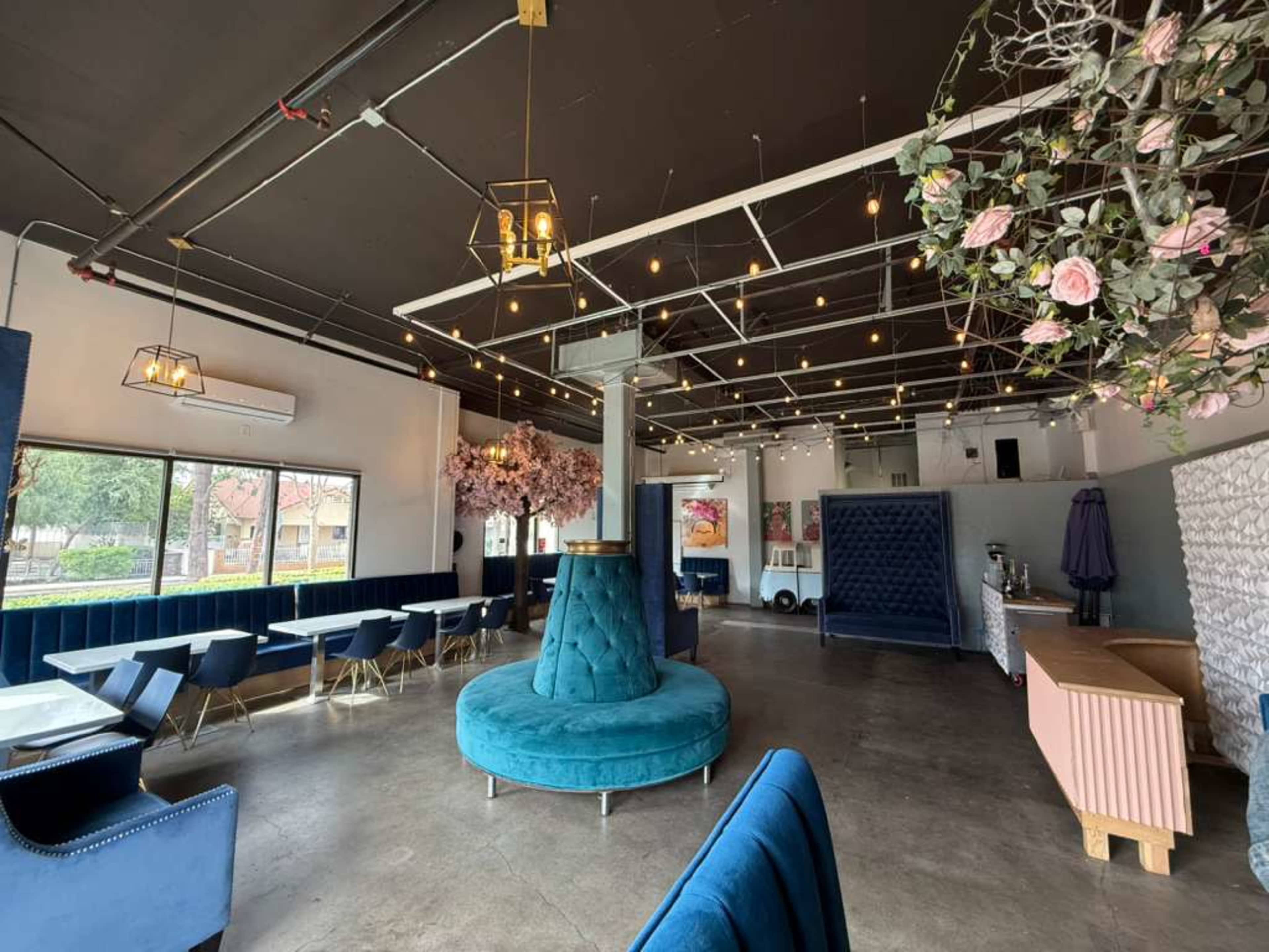 The image shows a modern café interior featuring blue furniture, pendant lights, and decorative plants.