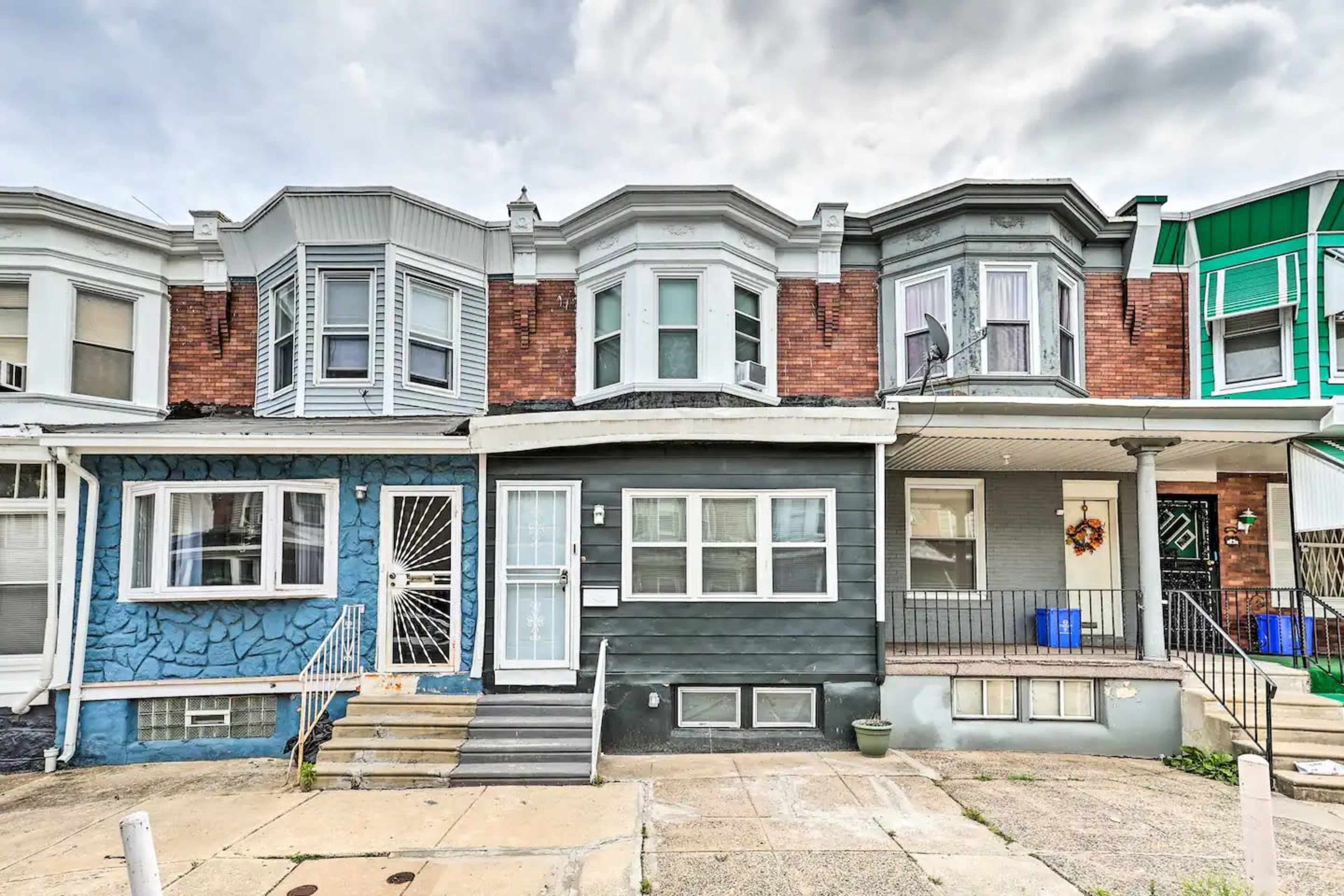 The image shows a row of three connected townhouses, featuring a mix of brick and painted siding, with various window styles and porch steps.