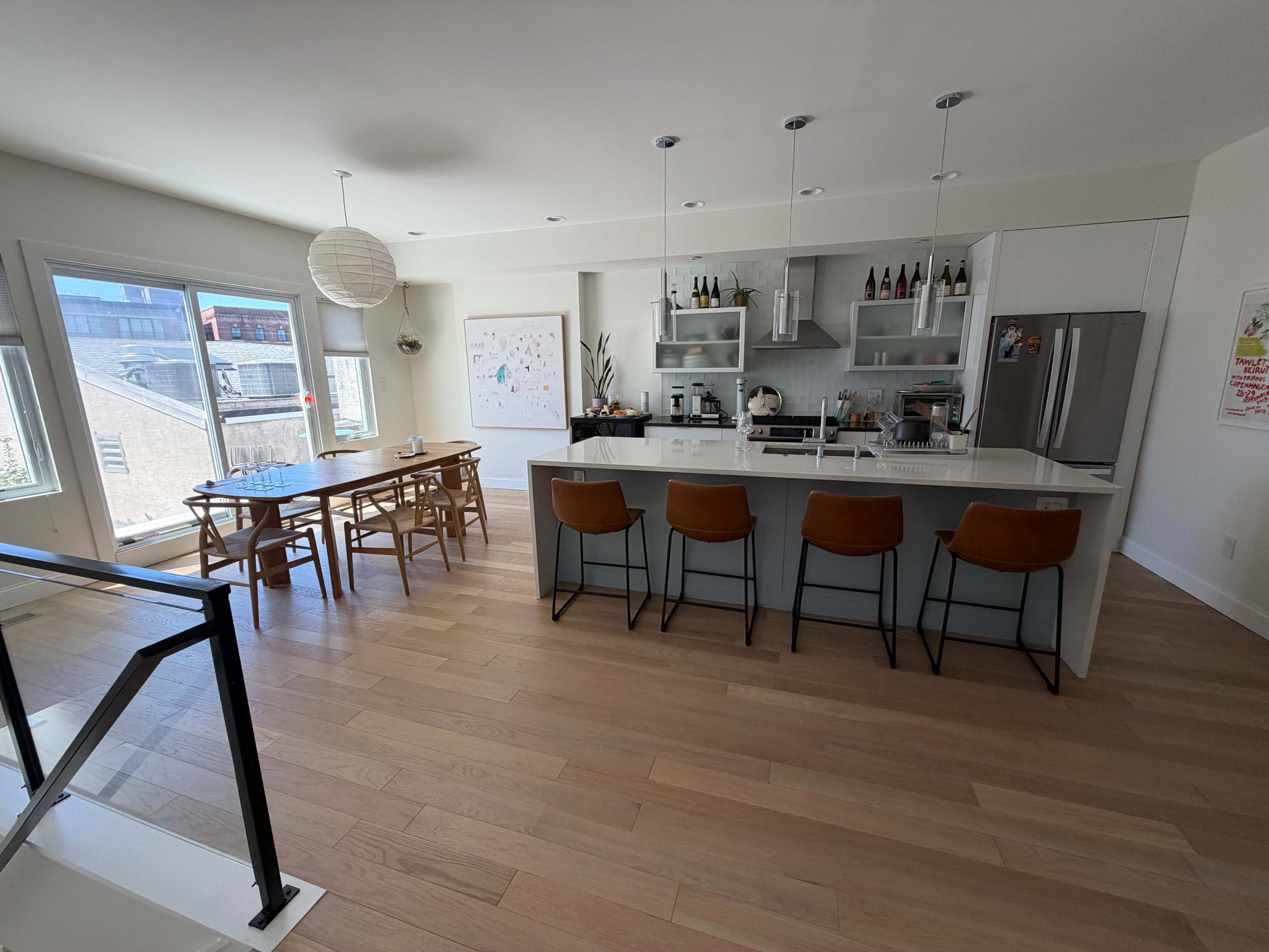The image shows a modern kitchen and dining area with a large island, wooden dining table, and several windows allowing natural light.