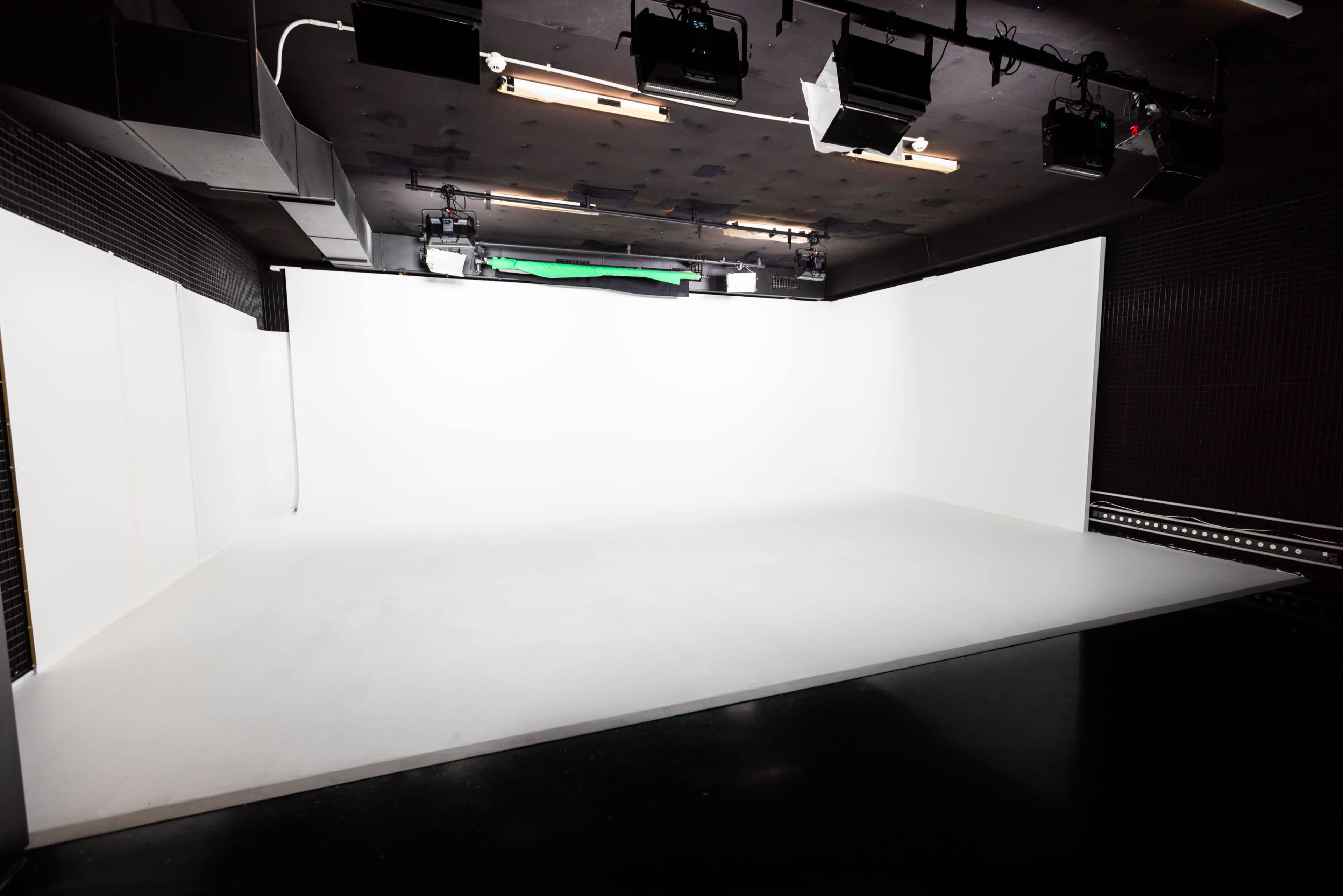 The image shows a spacious, empty studio with a white backdrop and overhead lighting.