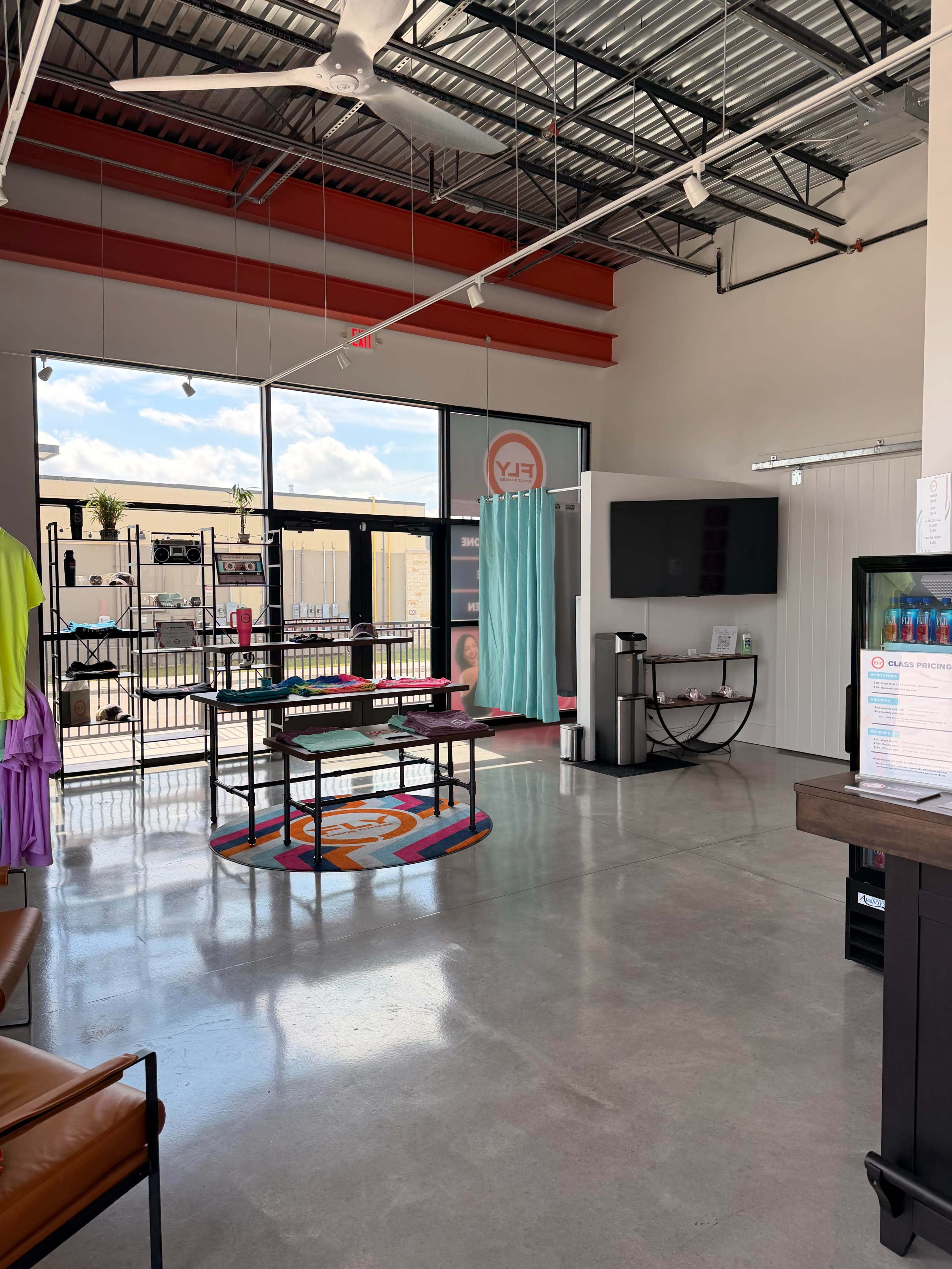 The image shows a spacious, modern retail space with large windows, a reception area, a TV, and clothing displays.