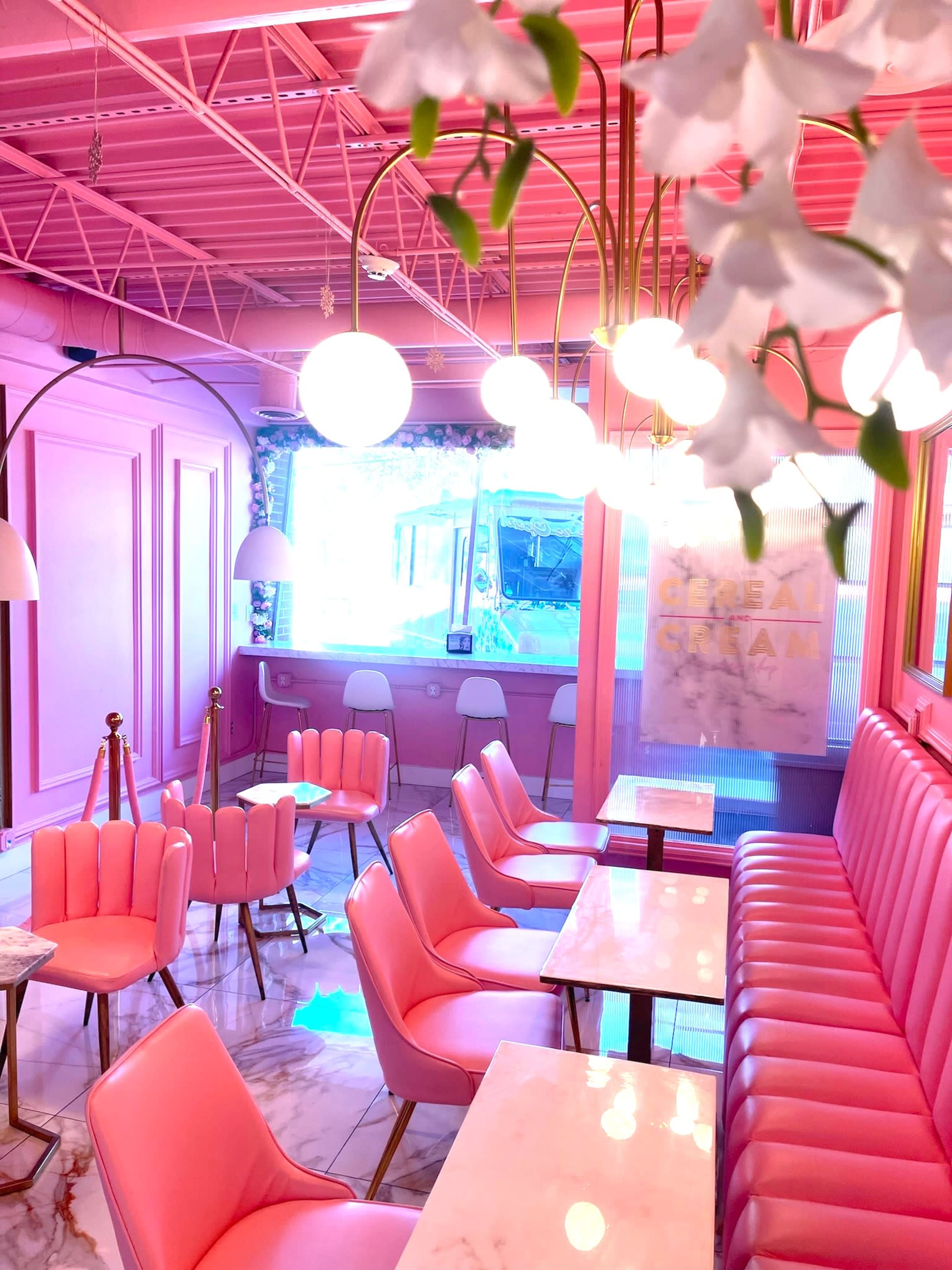 A brightly colored café interior featuring pink walls, pink seating, and round pendant lights.
