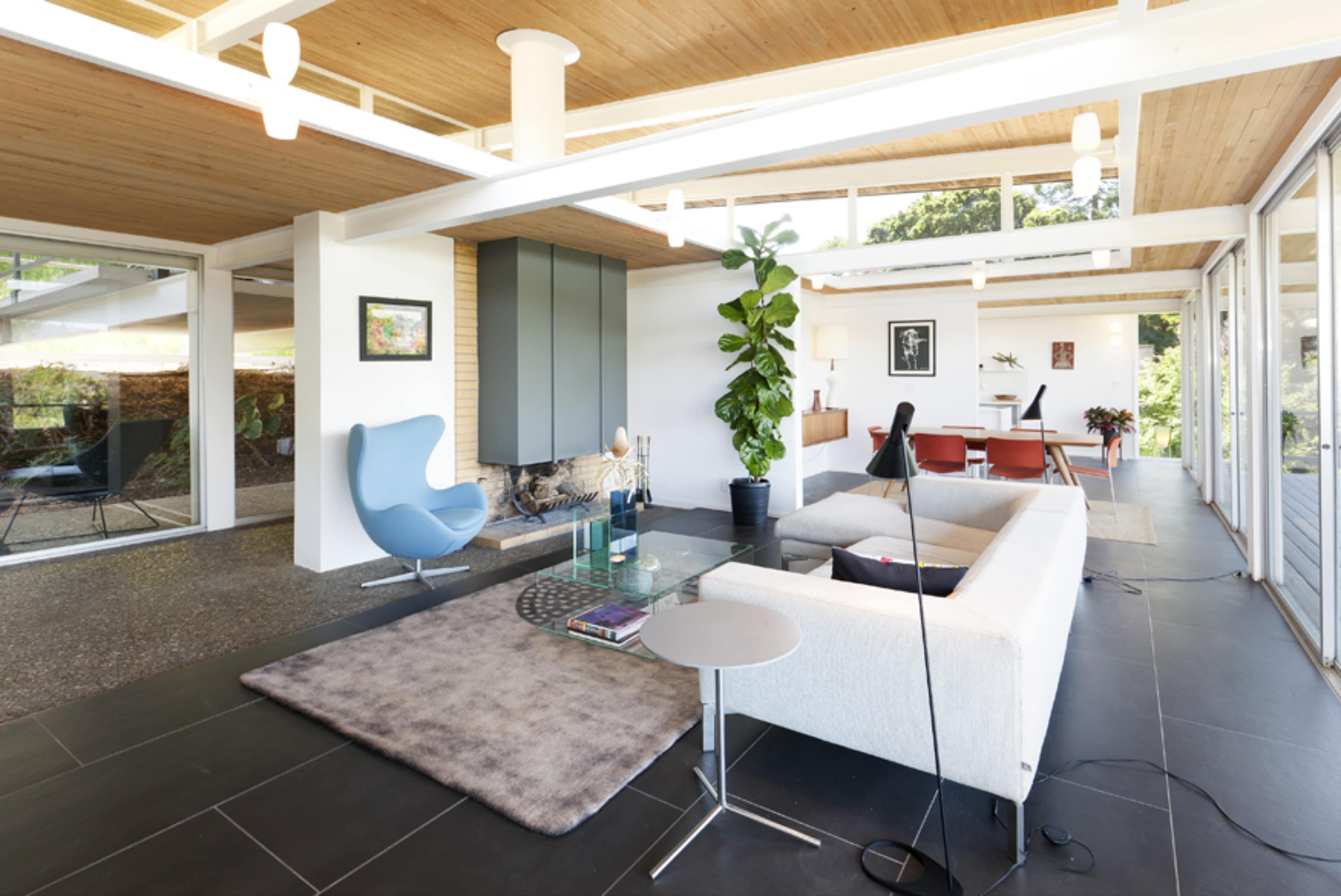 A modern living room with large windows, a minimalist design featuring a sofa, light fixtures, and indoor plants.