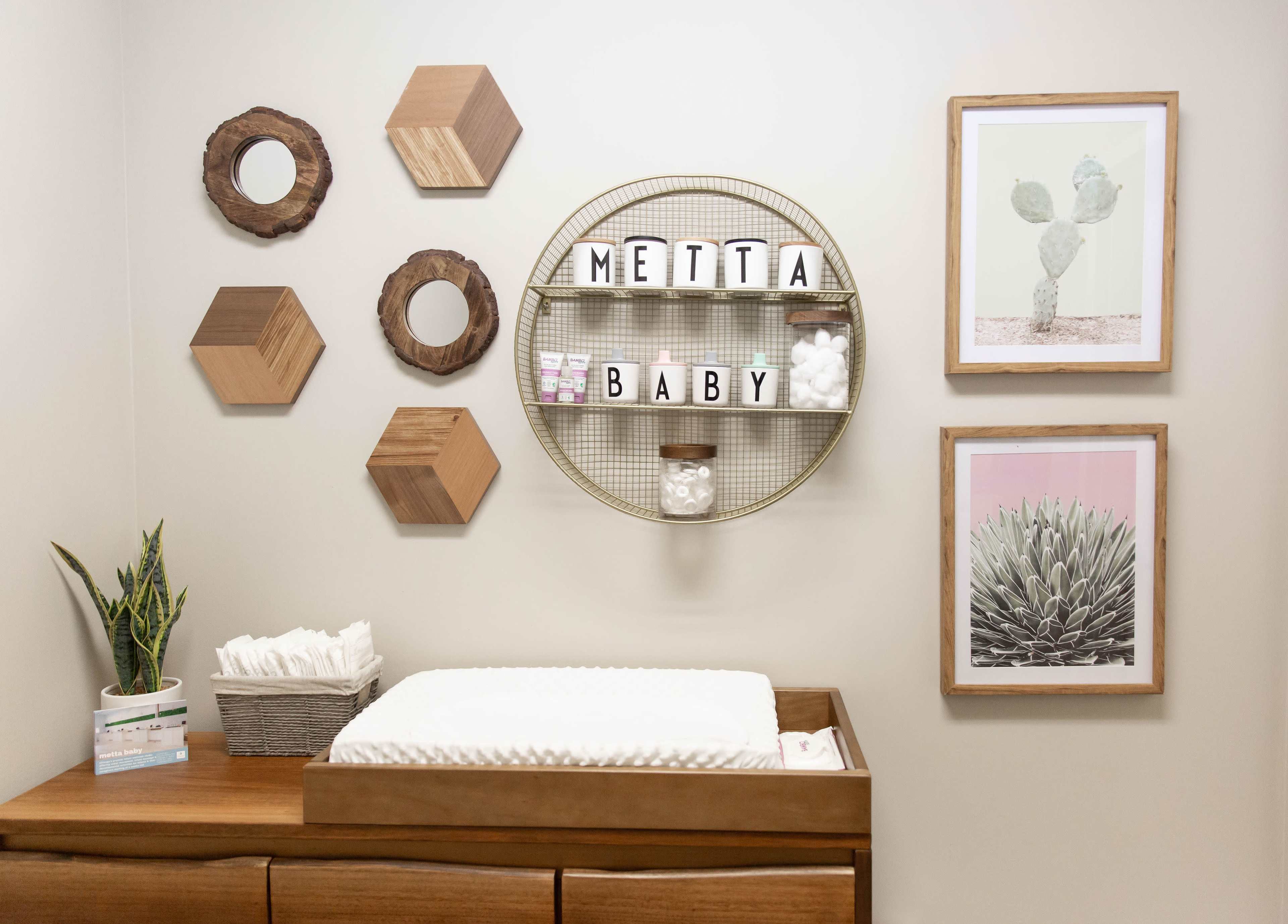 A modern nursery changing area with a wooden dresser, a changing pad, decorative wall shelves, and framed artwork featuring cacti.