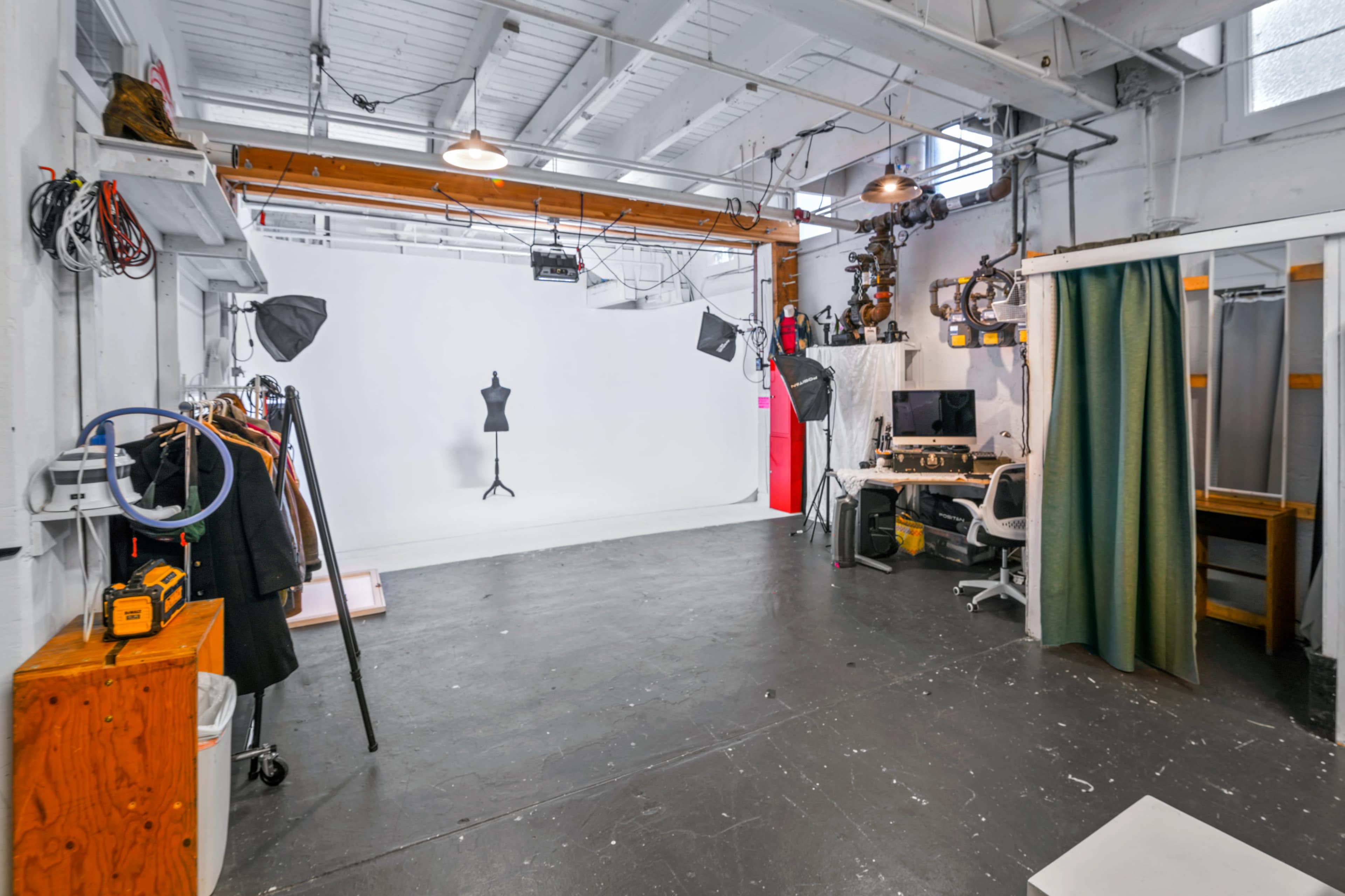 A photography studio with a blank white backdrop, lighting equipment, a dressing area, and a workspace with a computer.