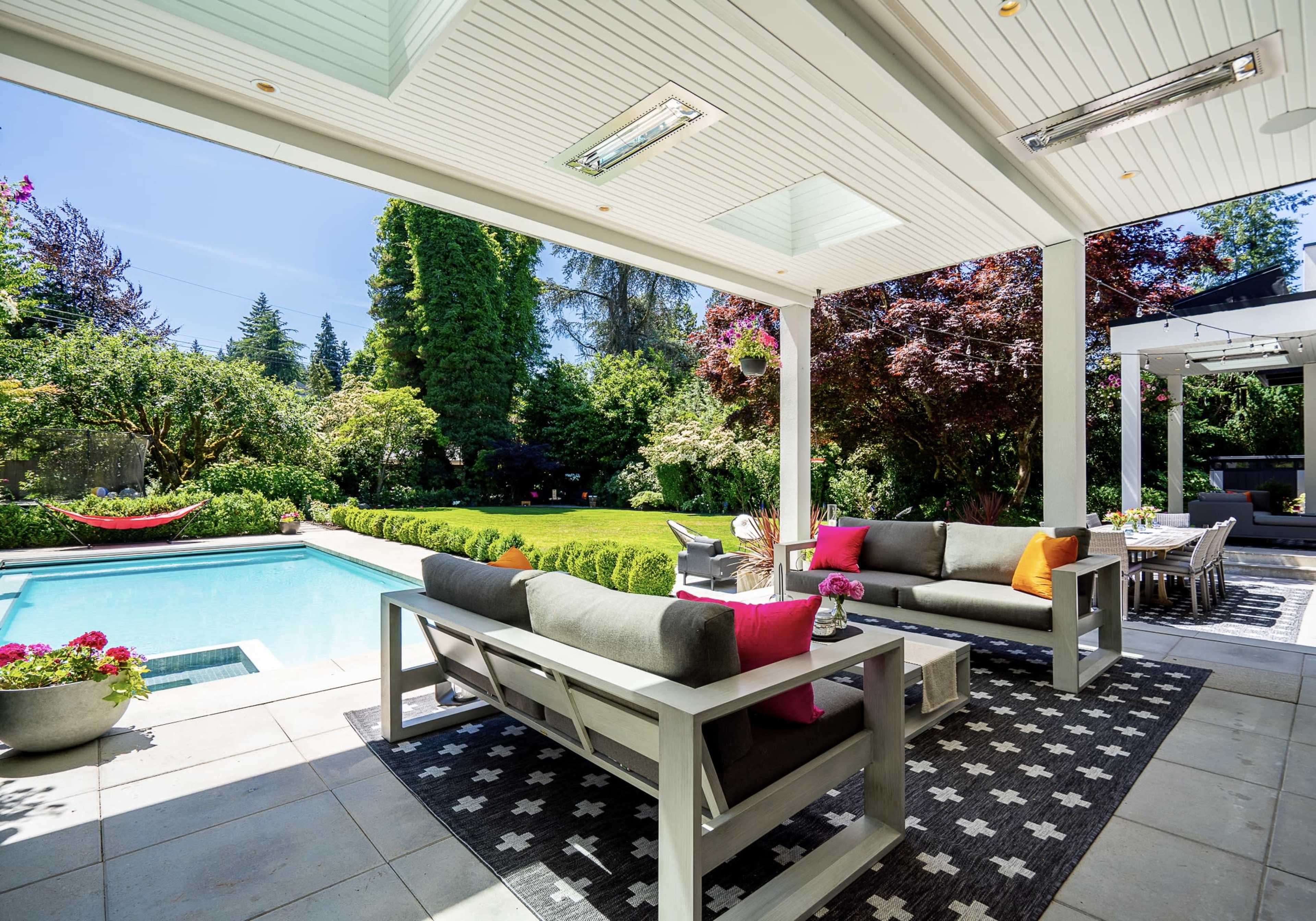 A modern patio area features a seating arrangement and a swimming pool surrounded by lush greenery and well-maintained landscaping.