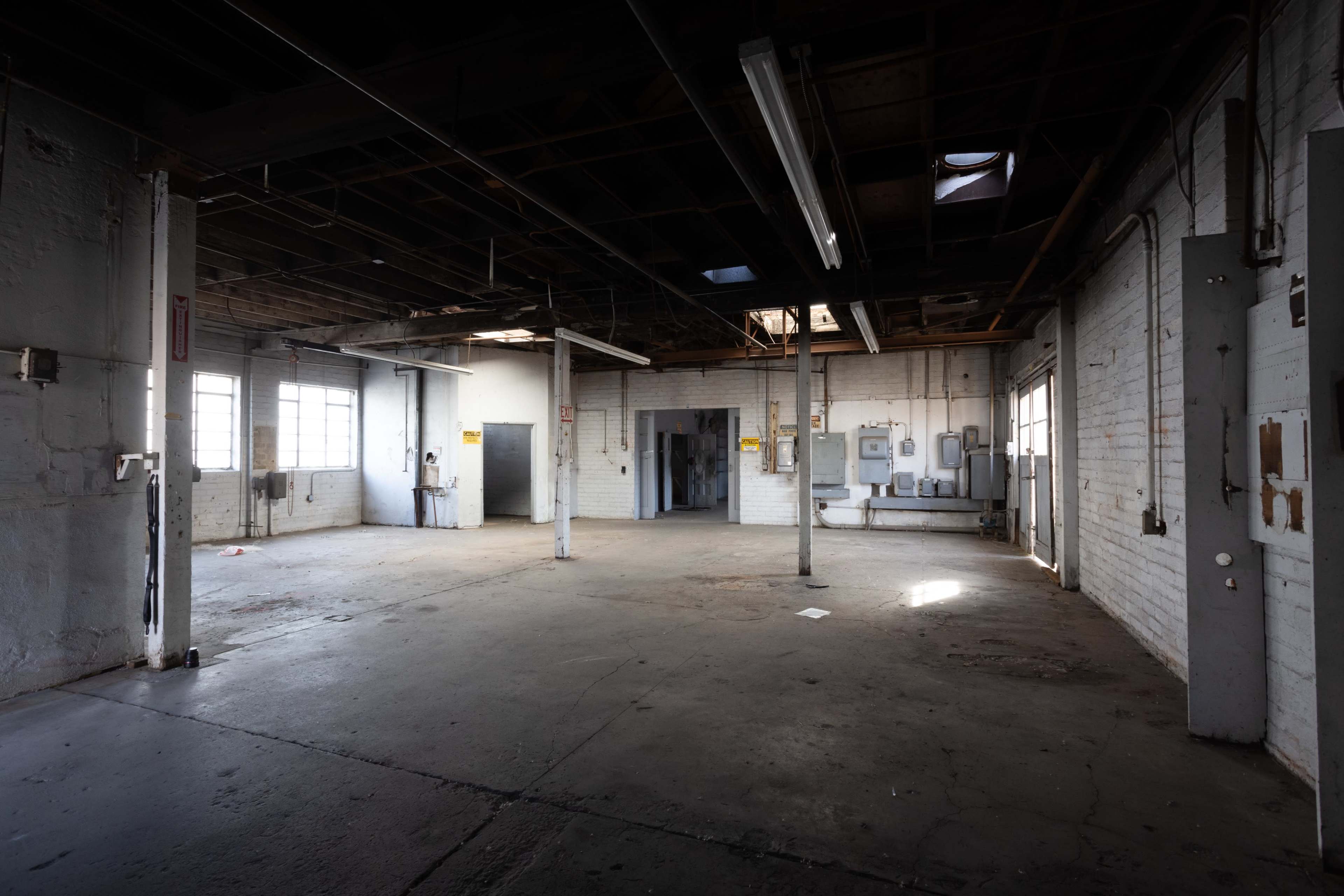 An empty industrial room with exposed beams, concrete flooring, and several windows allowing light to enter.