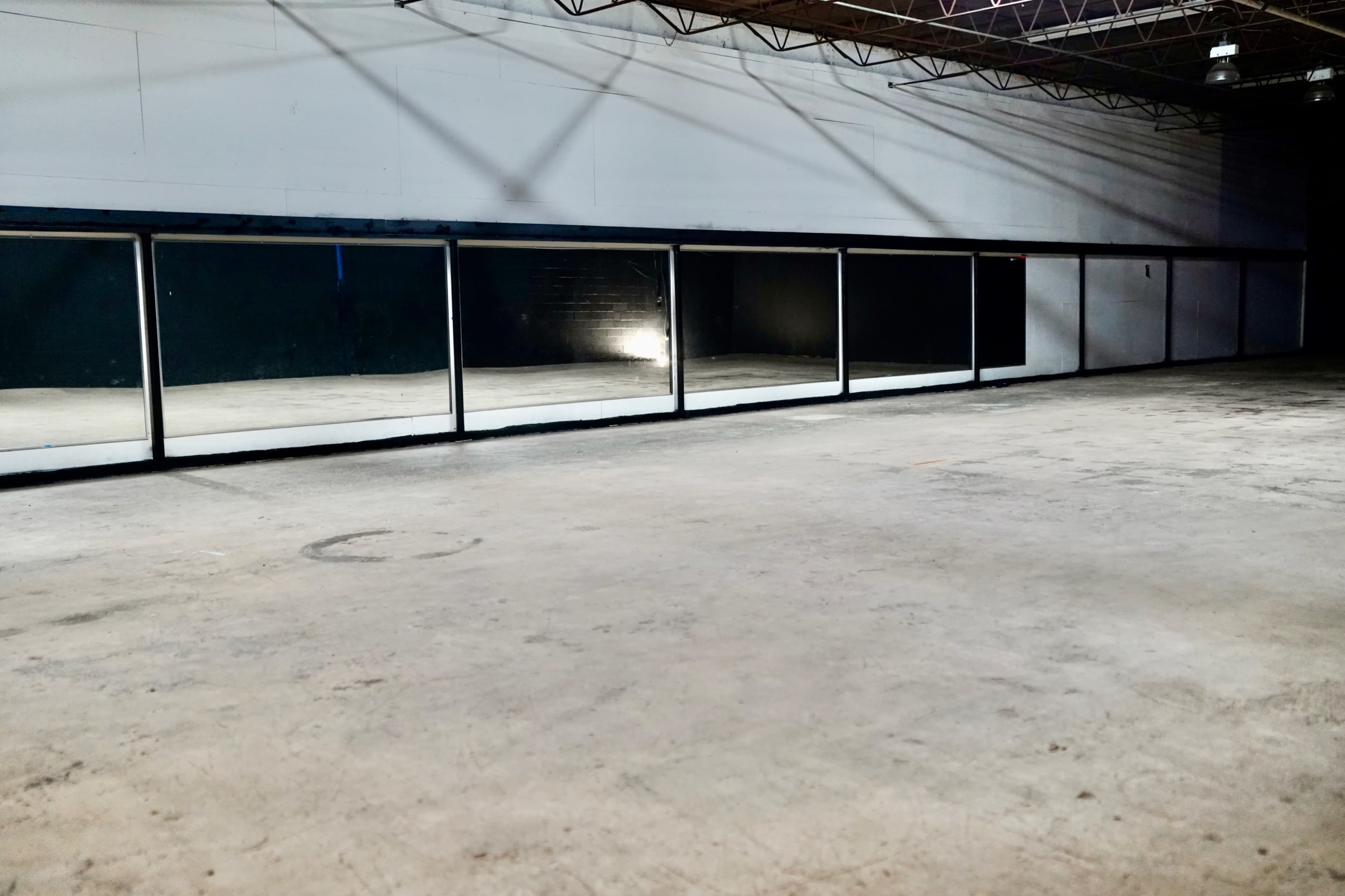 The image shows a large, empty room with a concrete floor and a row of mirrors along one wall.