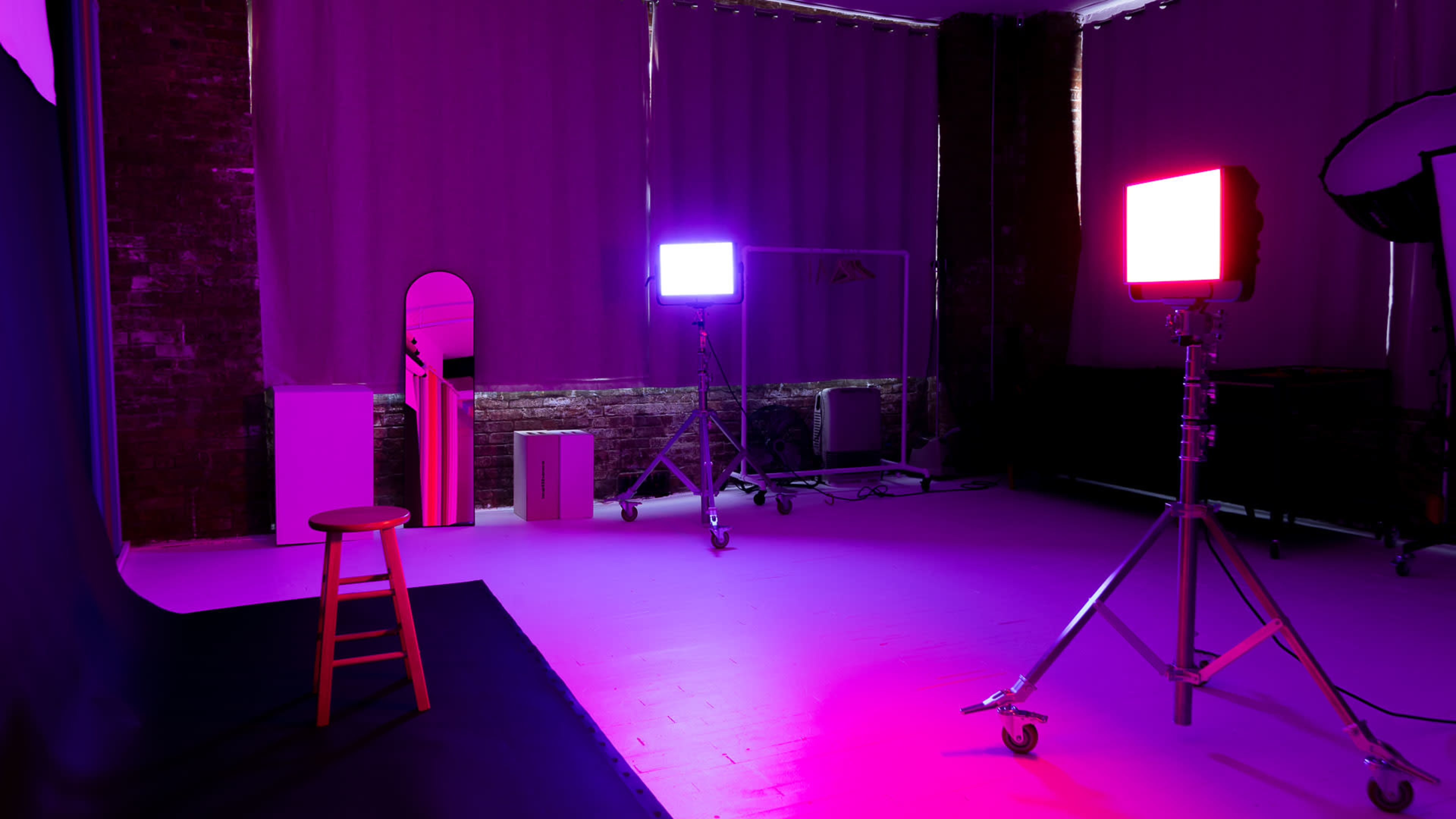 A photography studio features a stool illuminated by colorful lighting, with a mirror and equipment visible in the background.