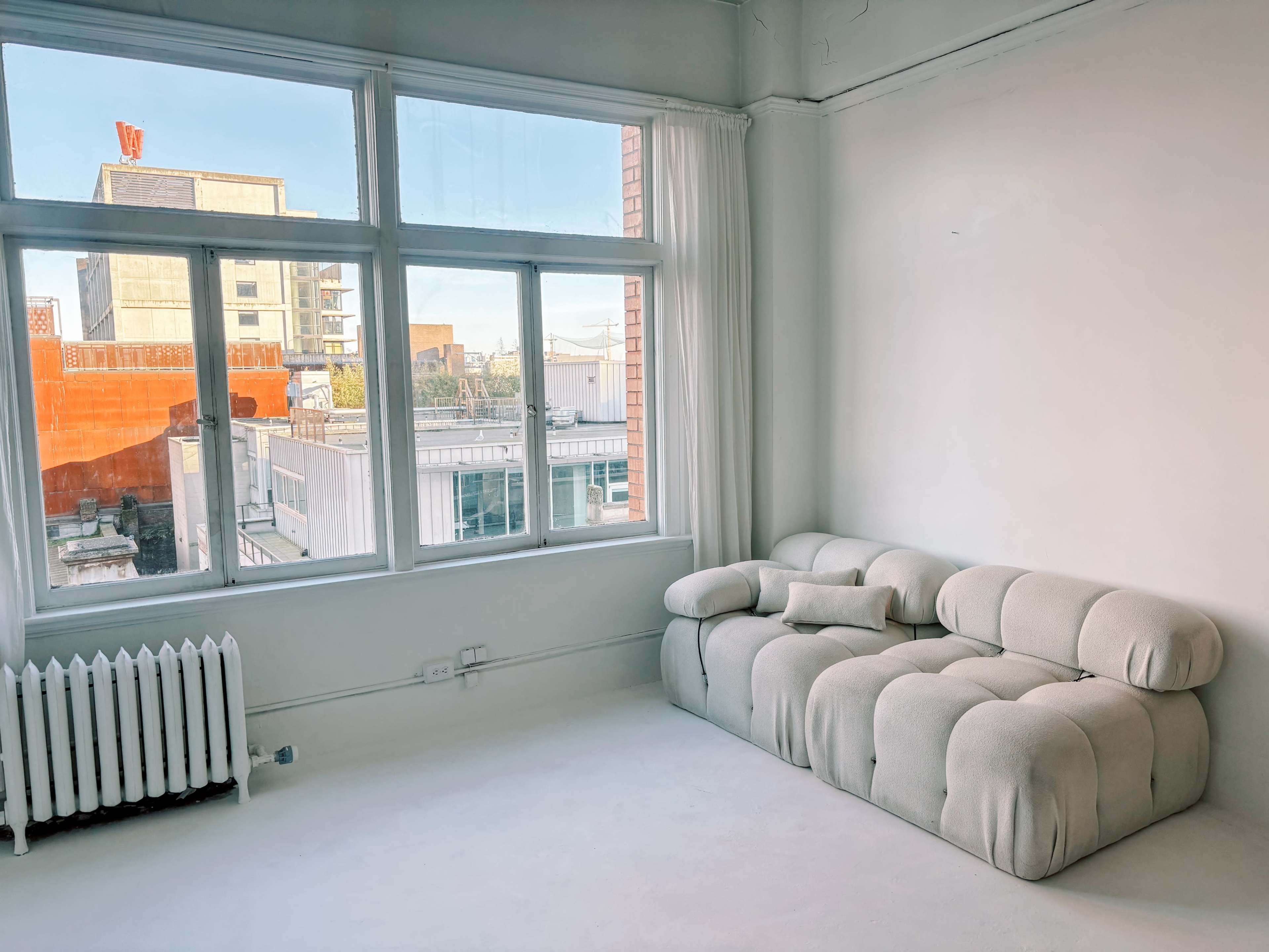 A minimalist room with a light-colored fabric sofa and large windows overlooking a cityscape.