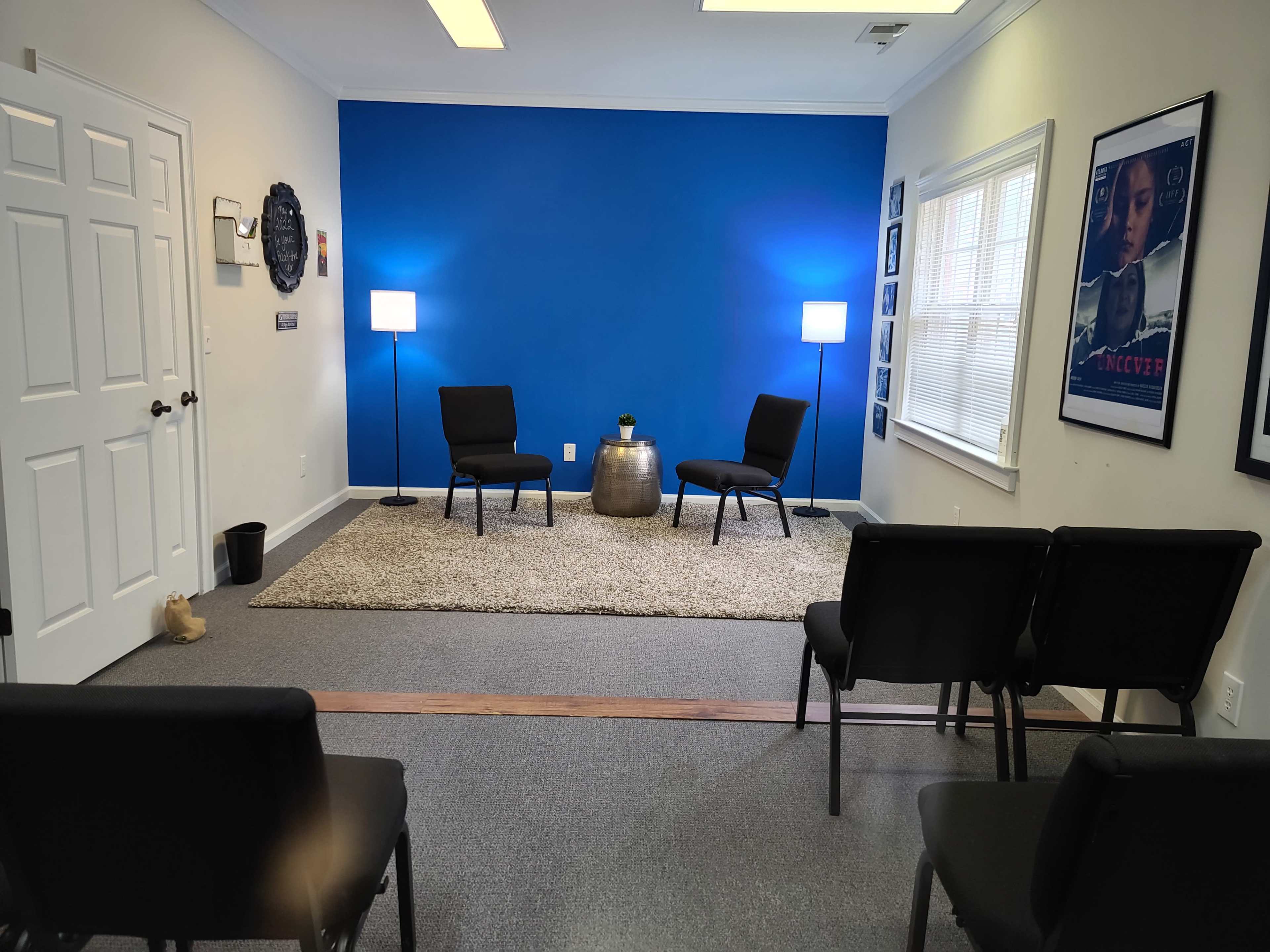 A room with a blue accent wall, two chairs facing a small table, and additional seating arranged in rows.